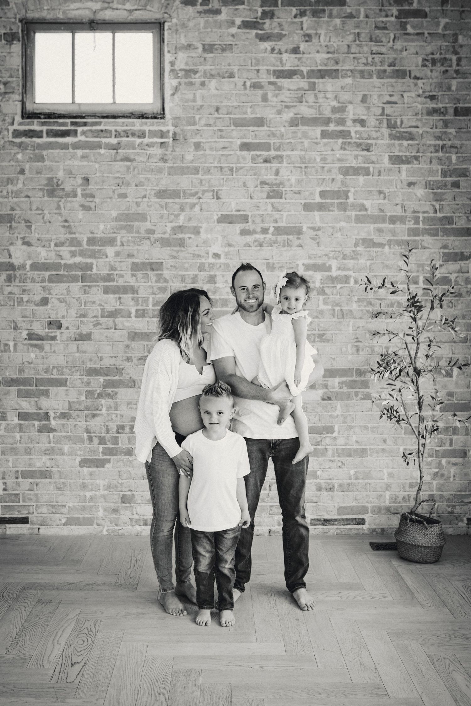 Black and white family portrait against brick wall with potted plant.