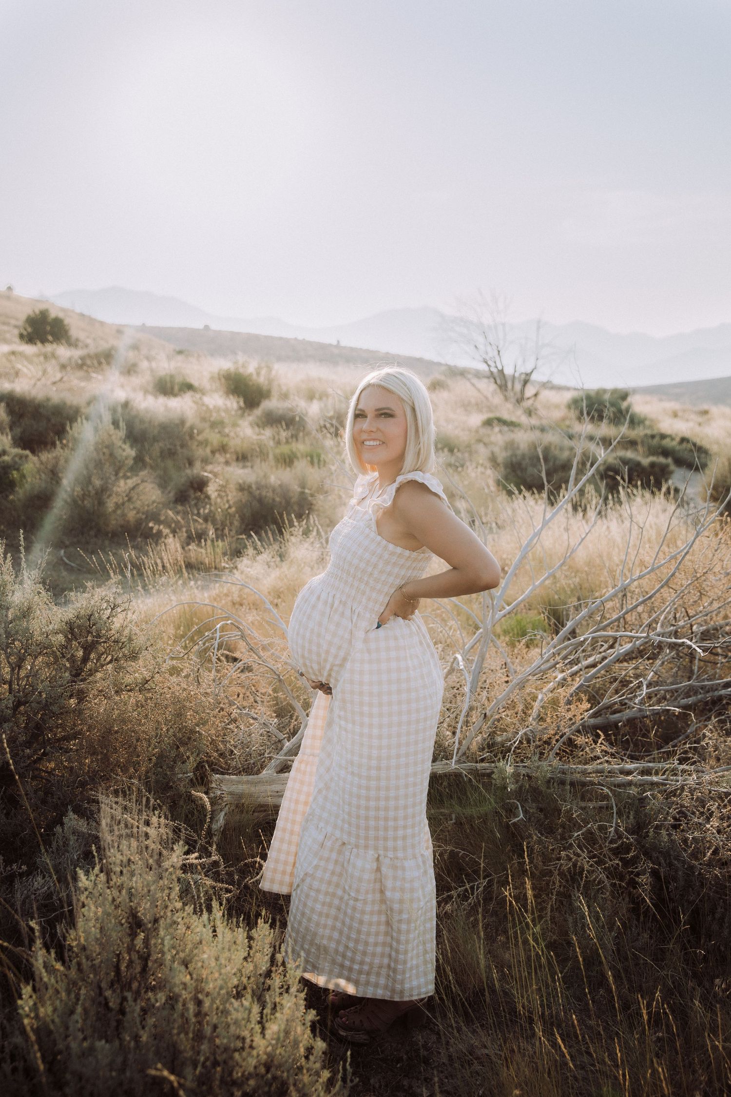 Woman in a checkered dress poses against desert brush and mountain backdrop.
