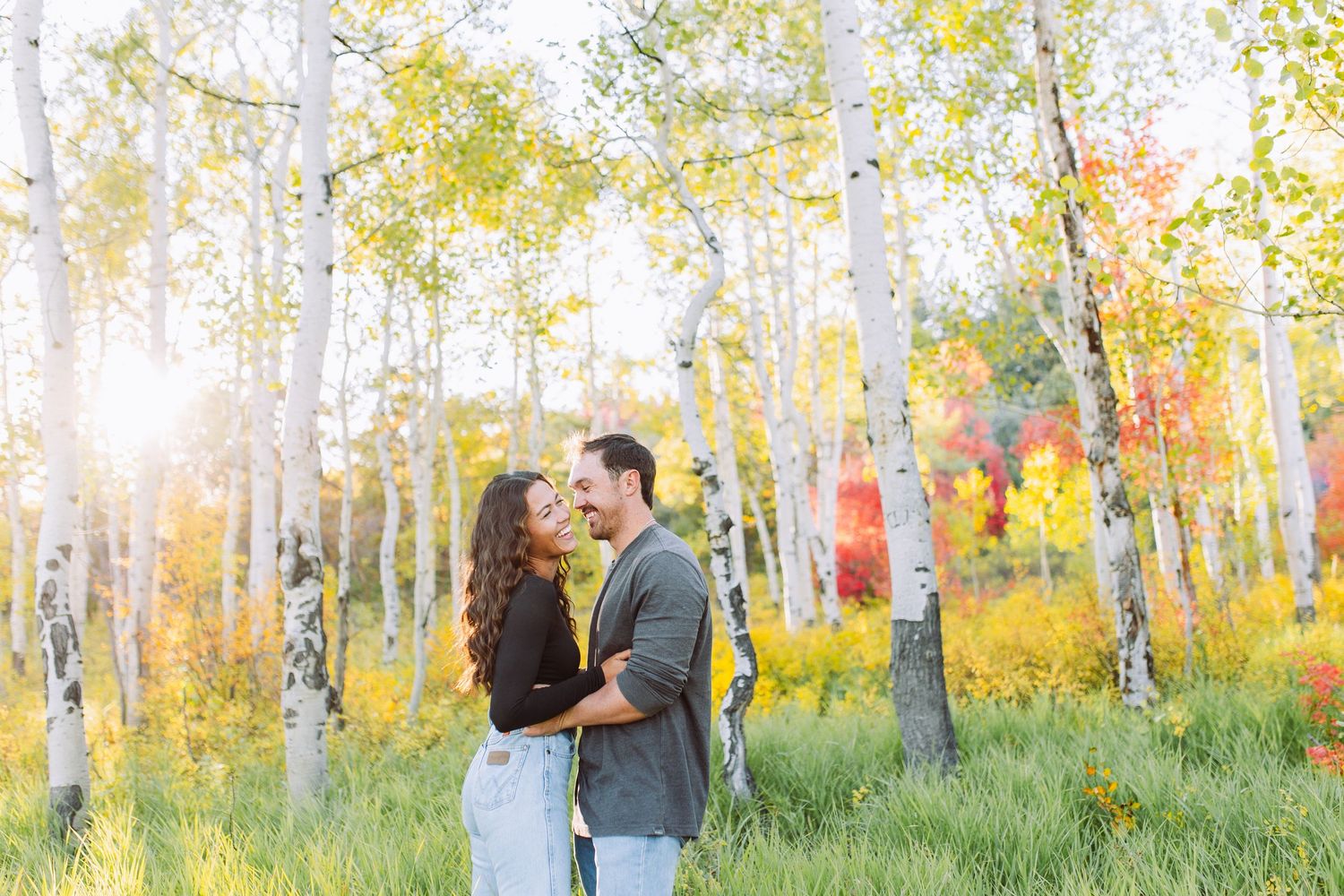 A couple shares an intimate moment among golden aspen trees in autumn sunlight.