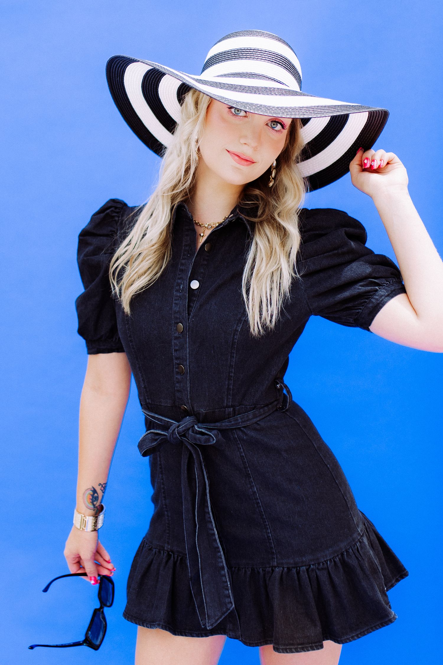 Black denim dress with bow detail and puff sleeves styled with wide brim striped hat.