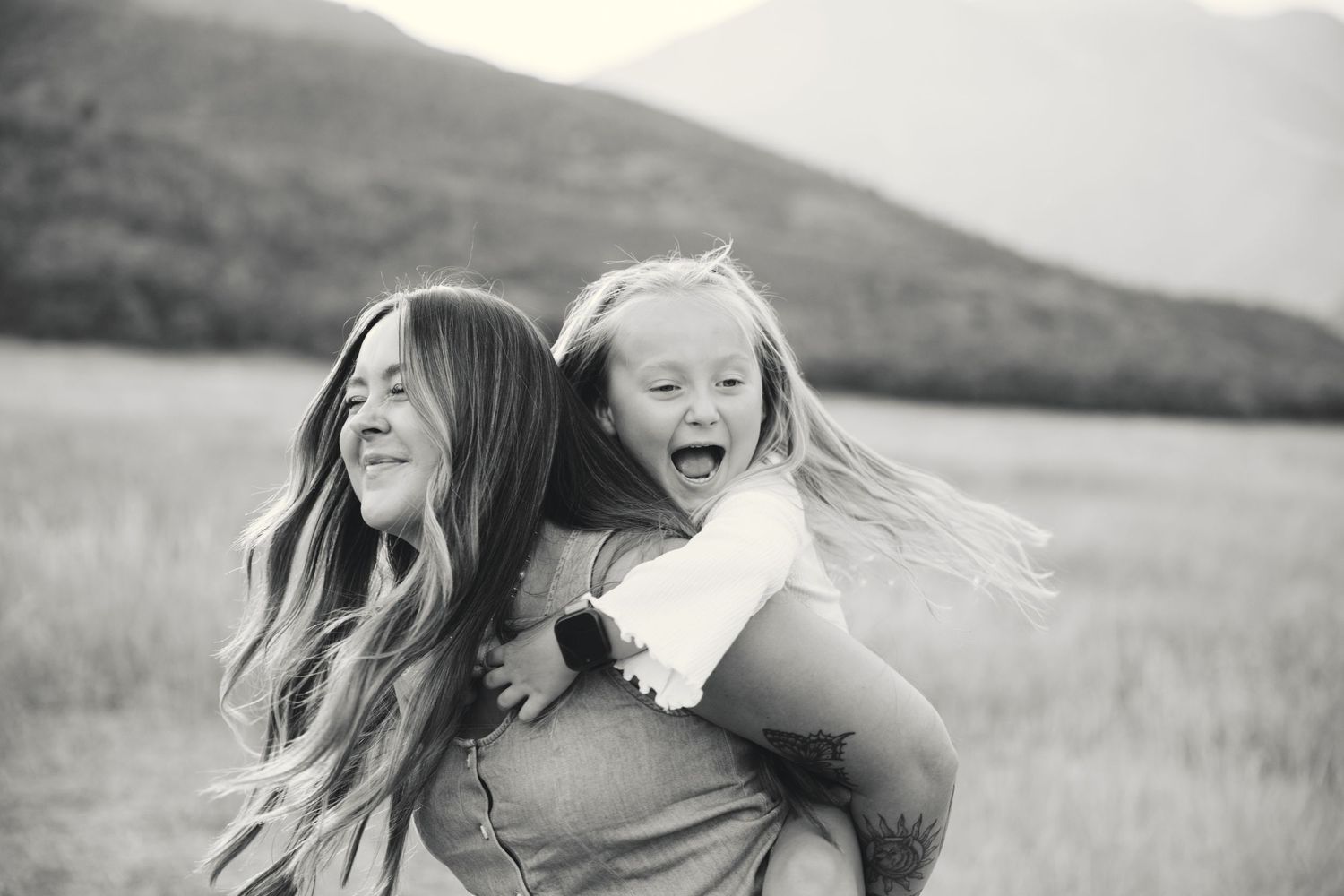 A black and white panoramic collage shows joyful moments between two people in a grassy field at sunset.