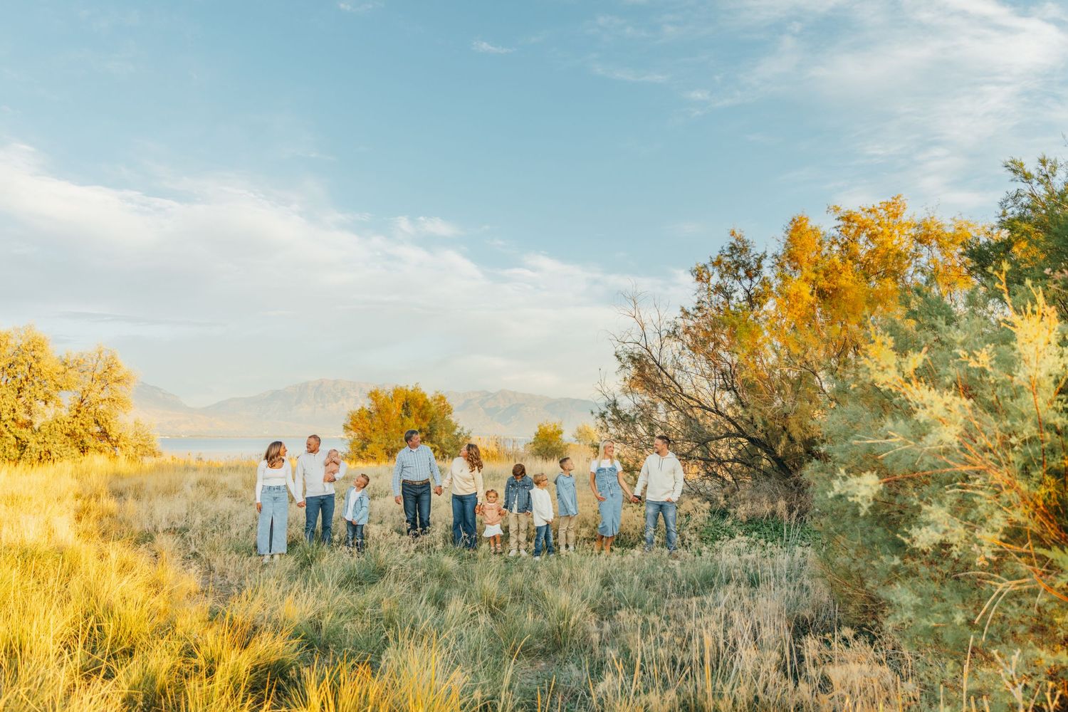 A panoramic sunset view of a group gathered in a golden field with autumn trees in the background.
