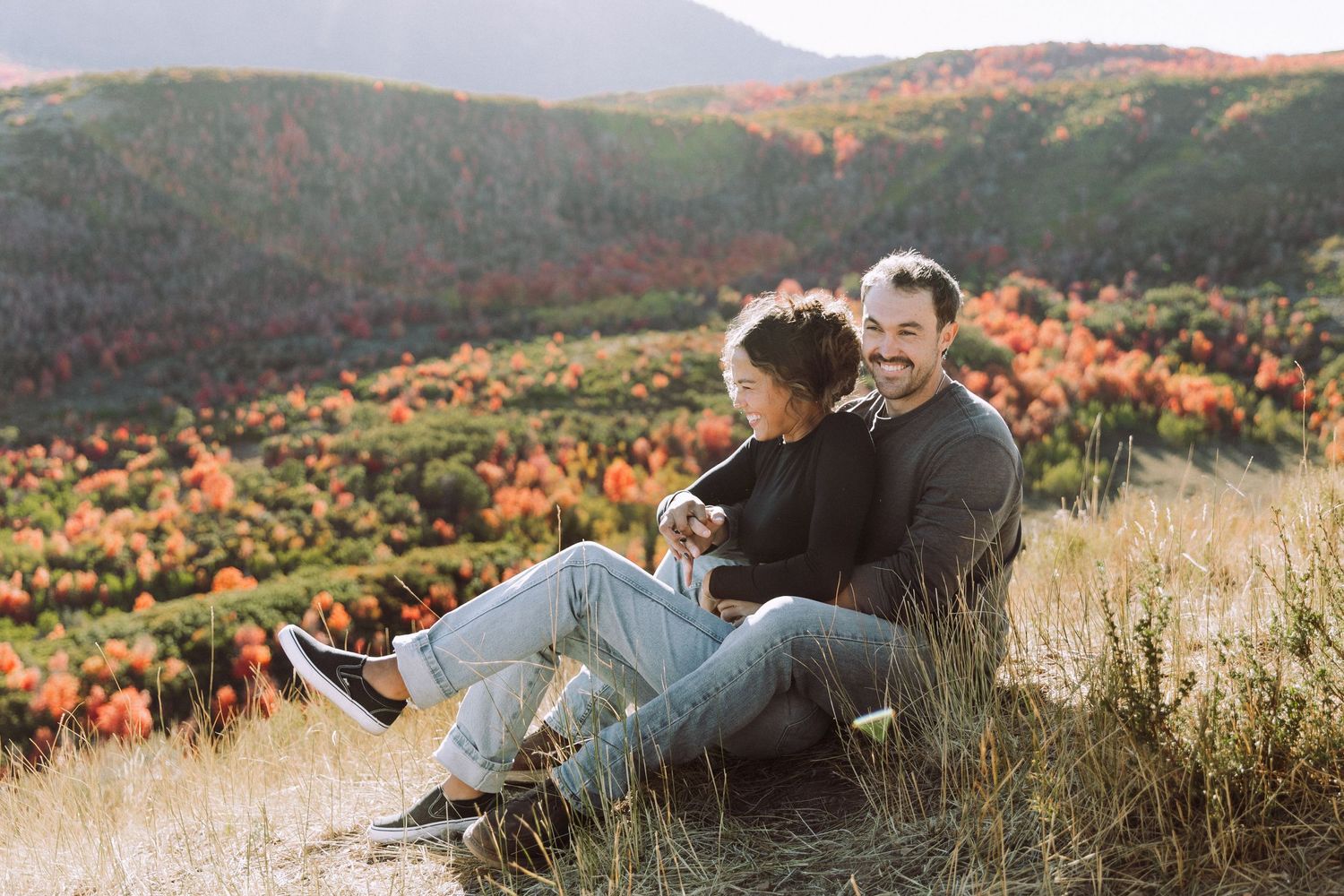 A couple relaxes together on a hilltop overlooking colorful fall foliage.