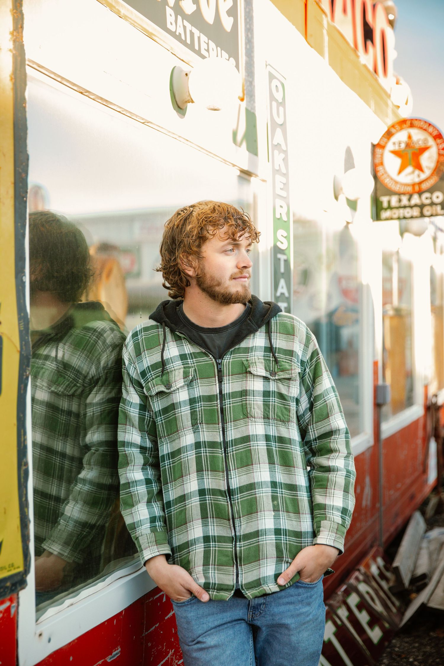 Person in green plaid flannel leans against vintage storefront windows.