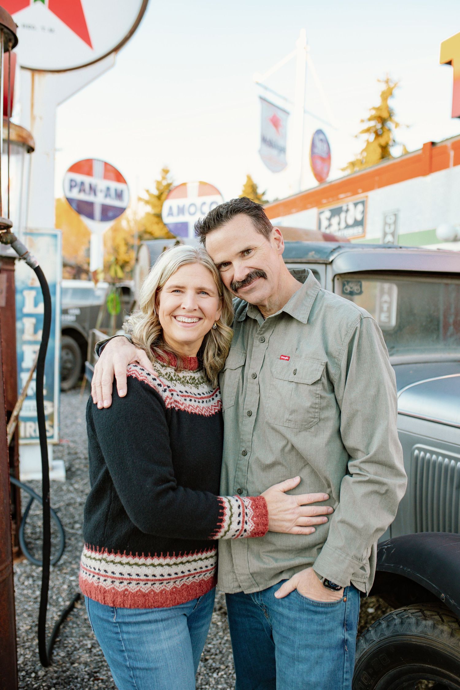 Couple wearing matching winter sweaters posing by vintage car.