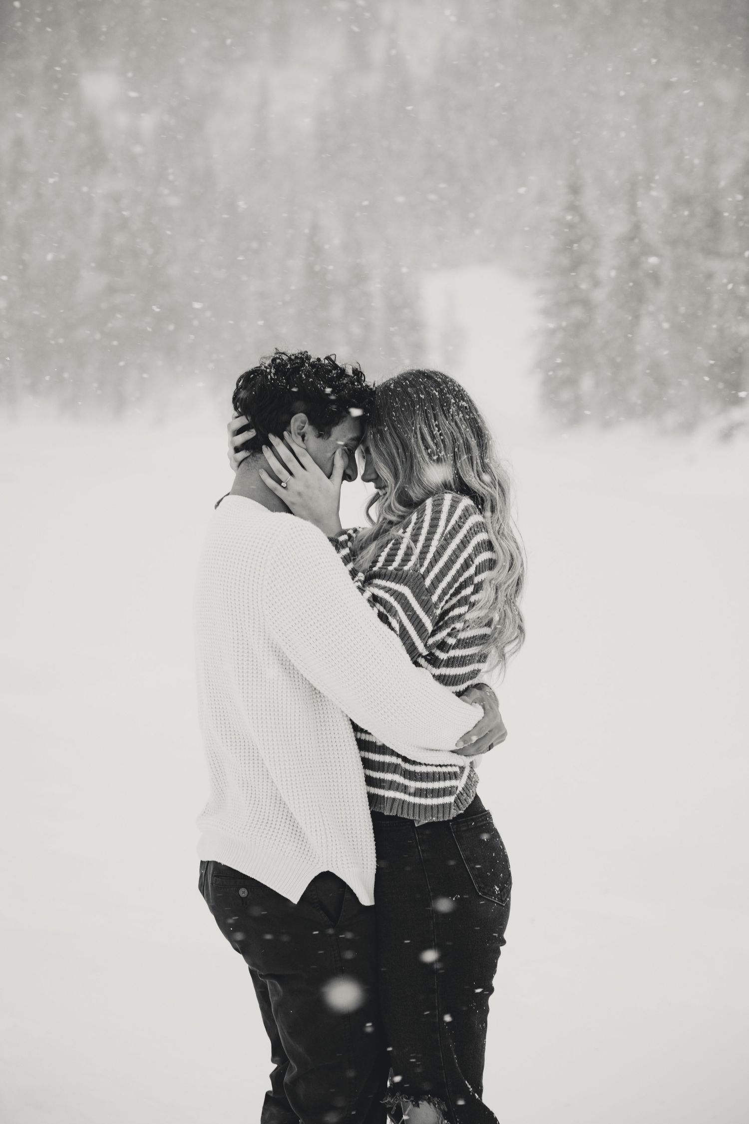 Two people share an intimate moment in the falling snow against a white winter backdrop.