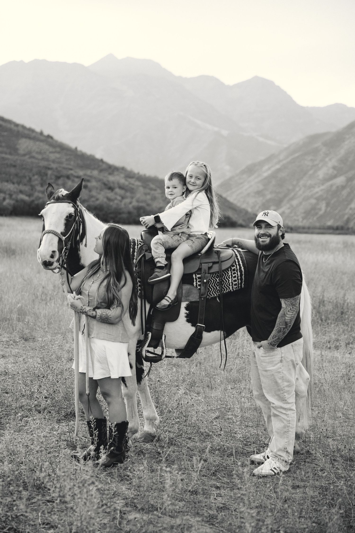 Family members playfully pose in a line behind a horse in a mountain meadow, creating a fun outdoor moment.