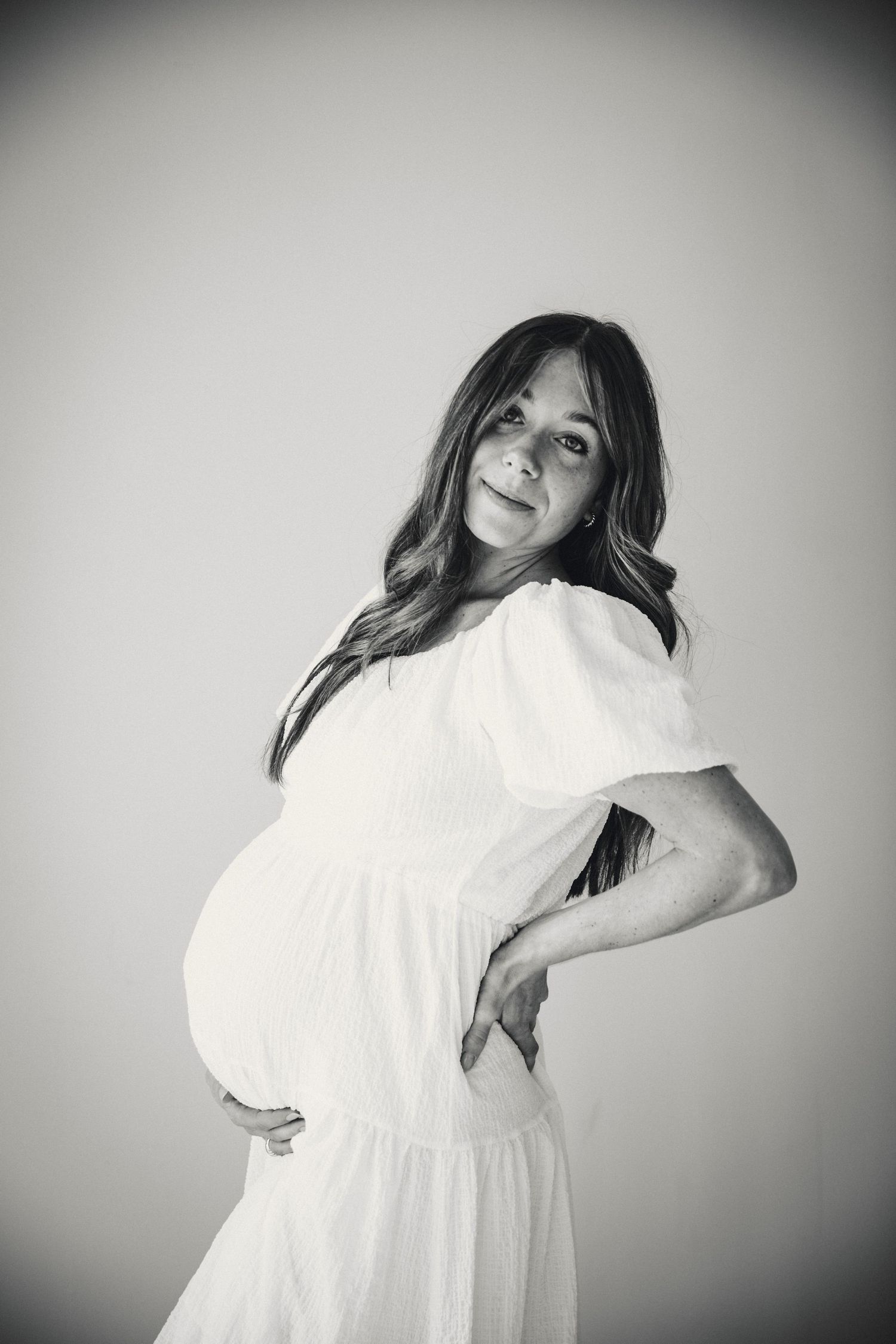 Artistic black and white maternity portraits with dynamic poses and flowing white dress.