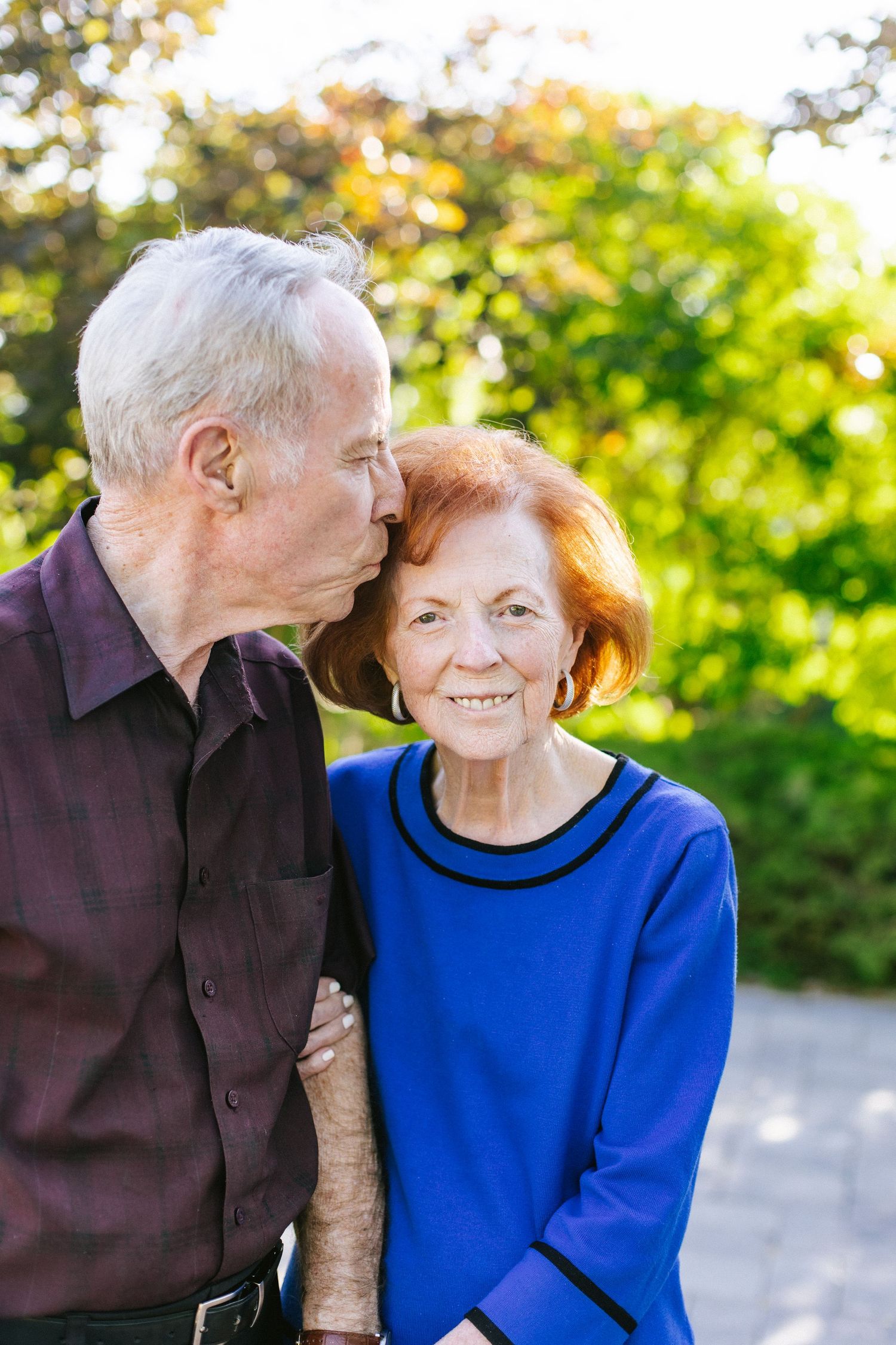 Elderly couple in blue and brown clothing sharing intimate moments in a sunny garden setting.