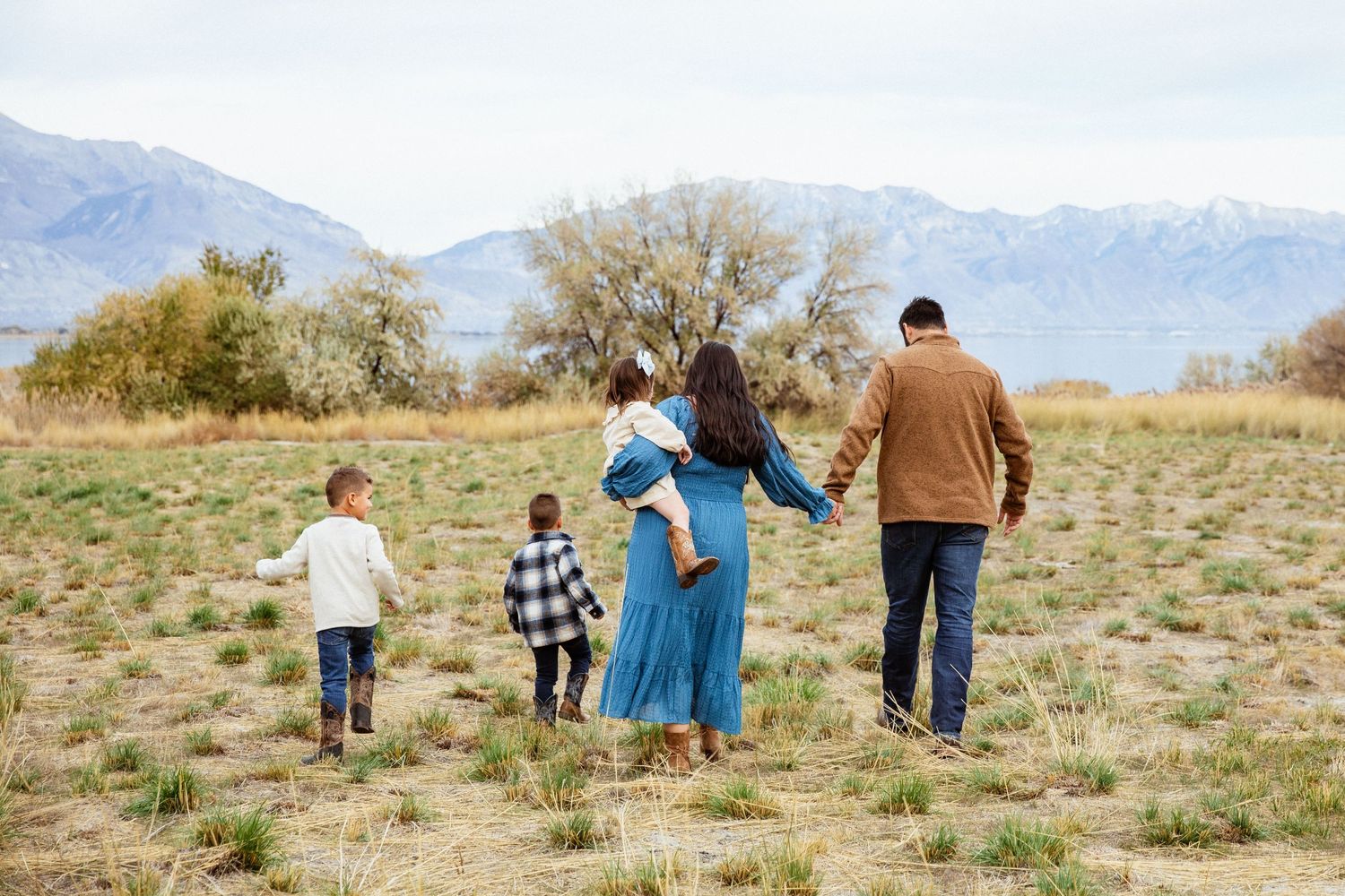 A family walks together in a grassy field with mountains in the background.