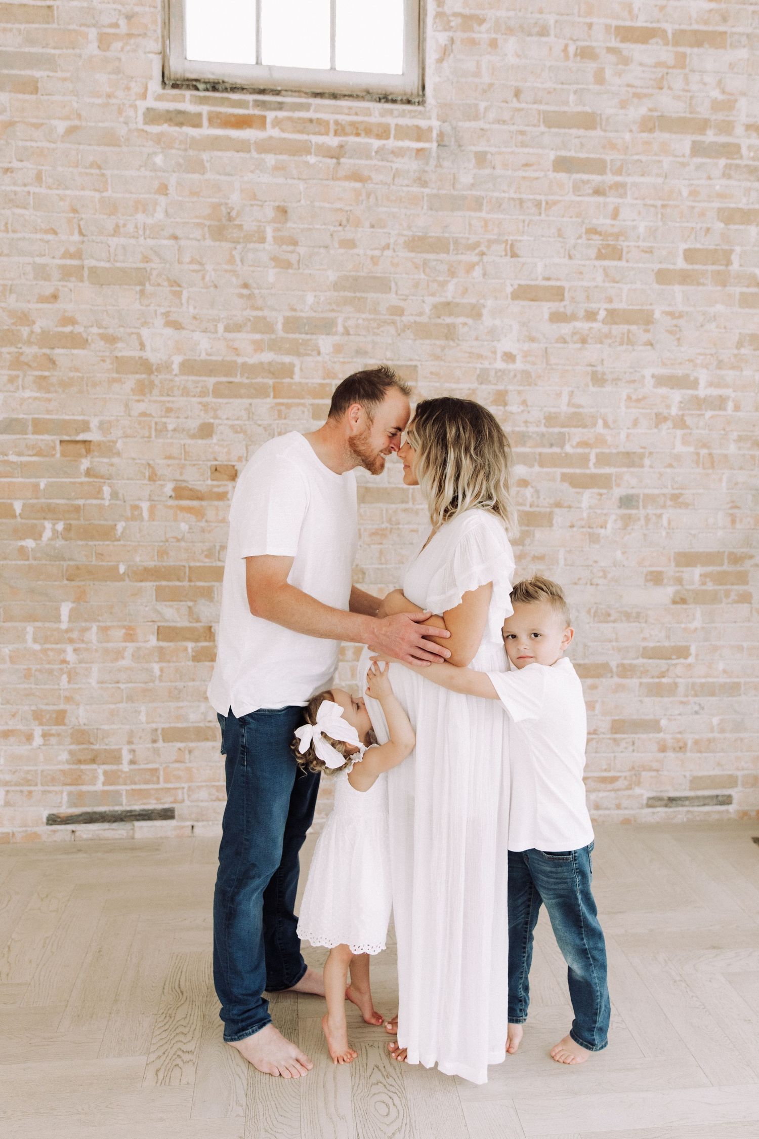 Tender family moment captured against rustic brick backdrop with children hugging.