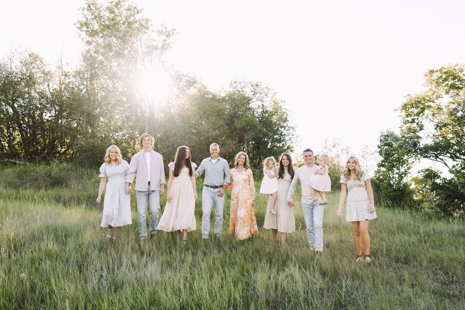 A group photo of people wearing coordinated white and neutral outfits in a sunlit meadow.
