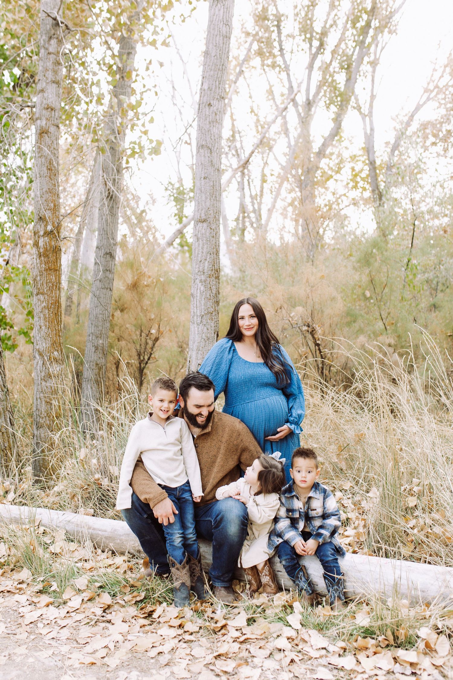 Family sitting together on fallen tree trunk during autumn outdoor photoshoot.