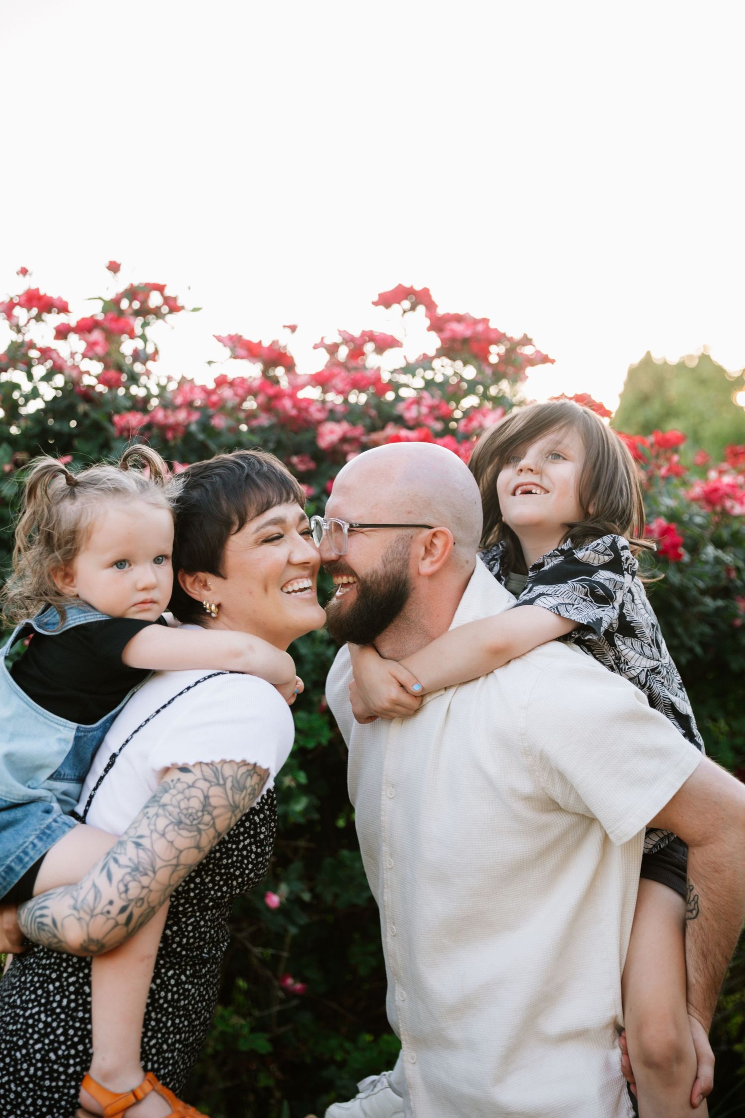 A family shares joyful moments together against a backdrop of pink flowering bushes in a garden setting.