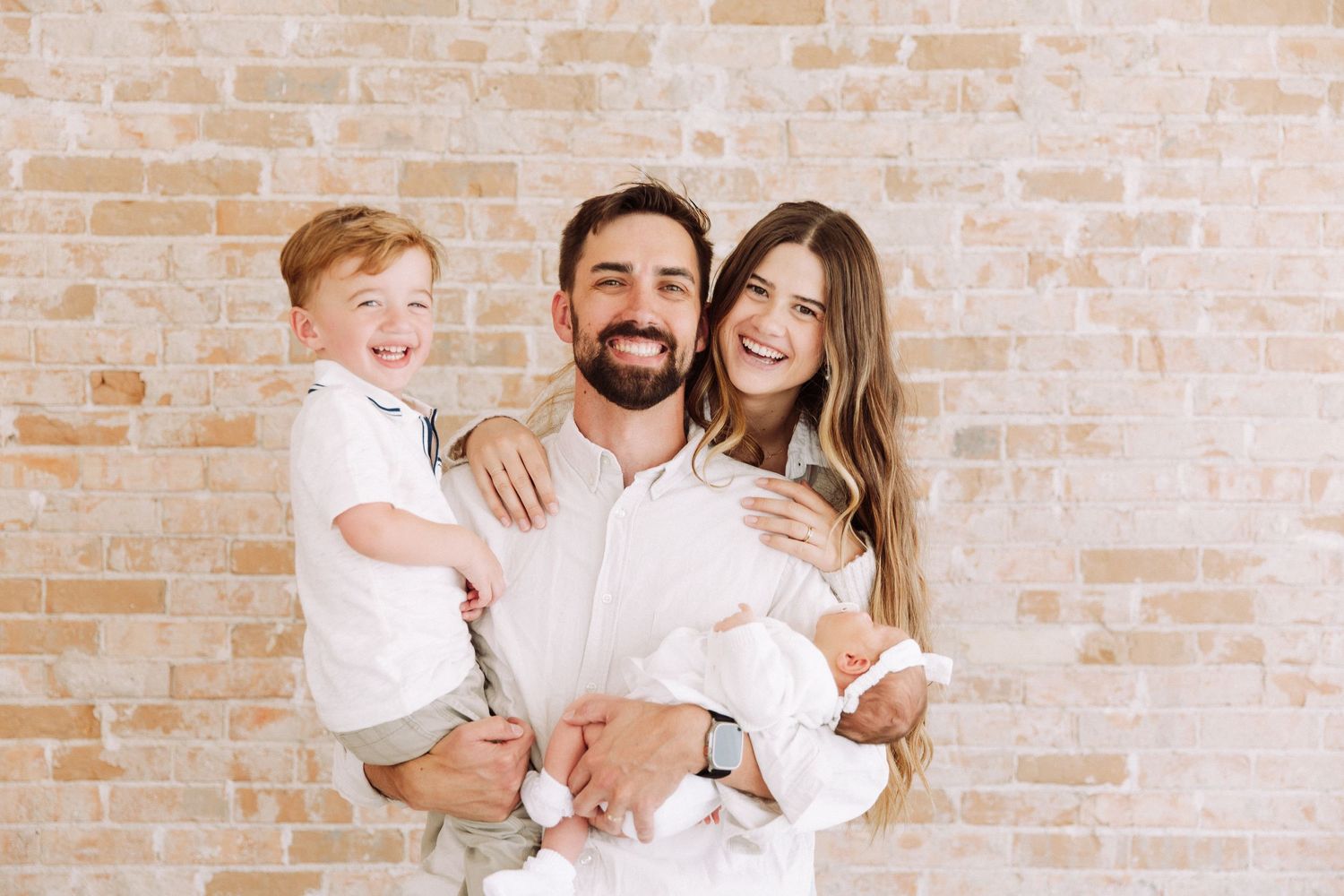 Happy family portrait series against warm brick wall backdrop.