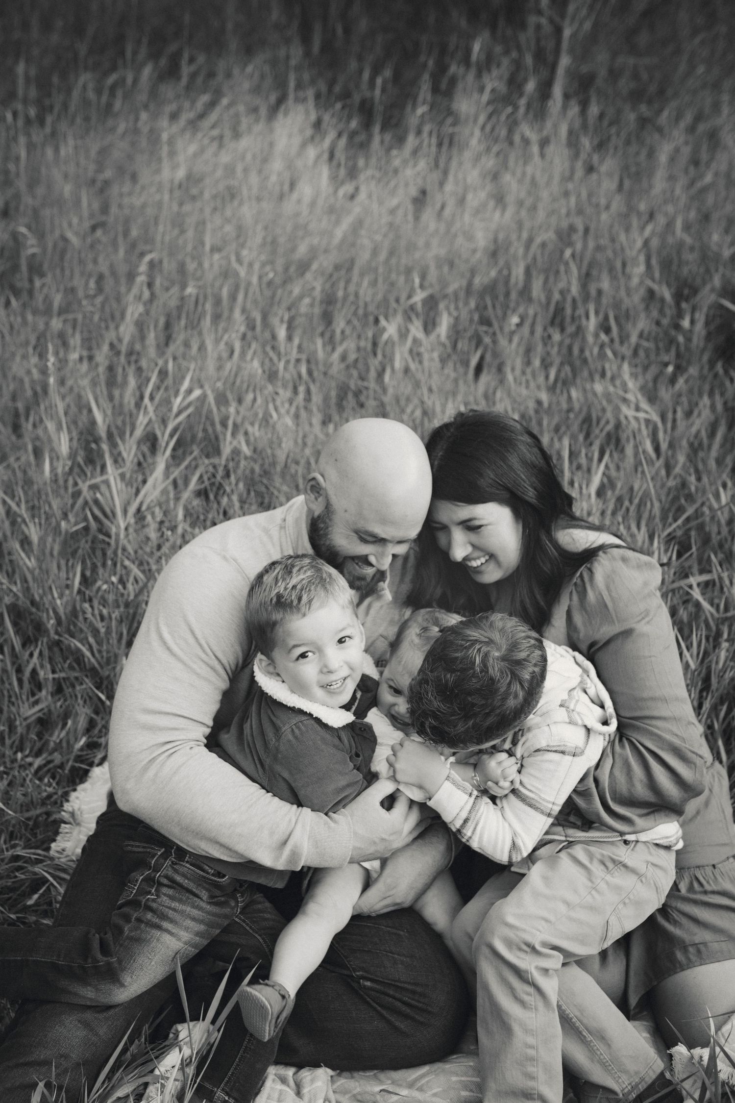 A black and white family portrait taken outdoors in a field of tall grass.