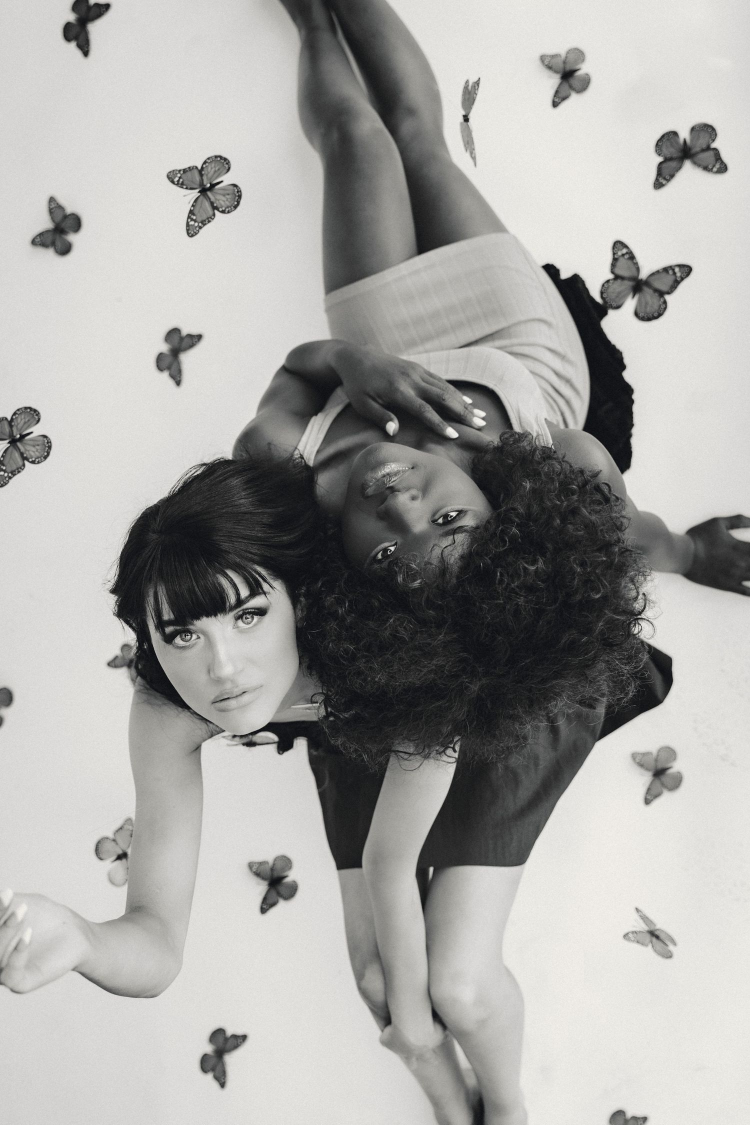 Artistic black and white photo with models lying down surrounded by butterfly decorations.