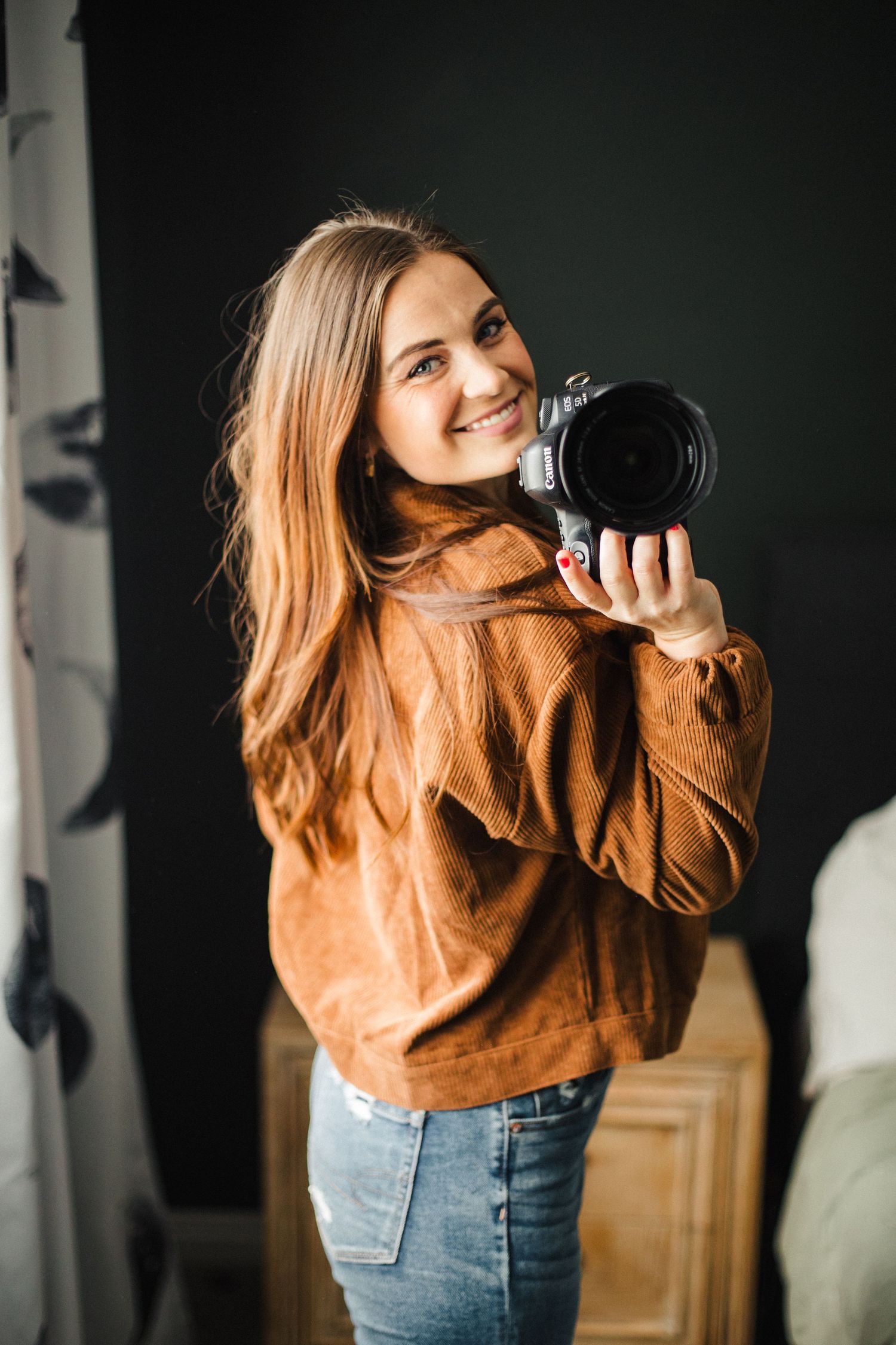 Photographer in brown sweater and jeans takes photos with professional camera in dramatic lighting.