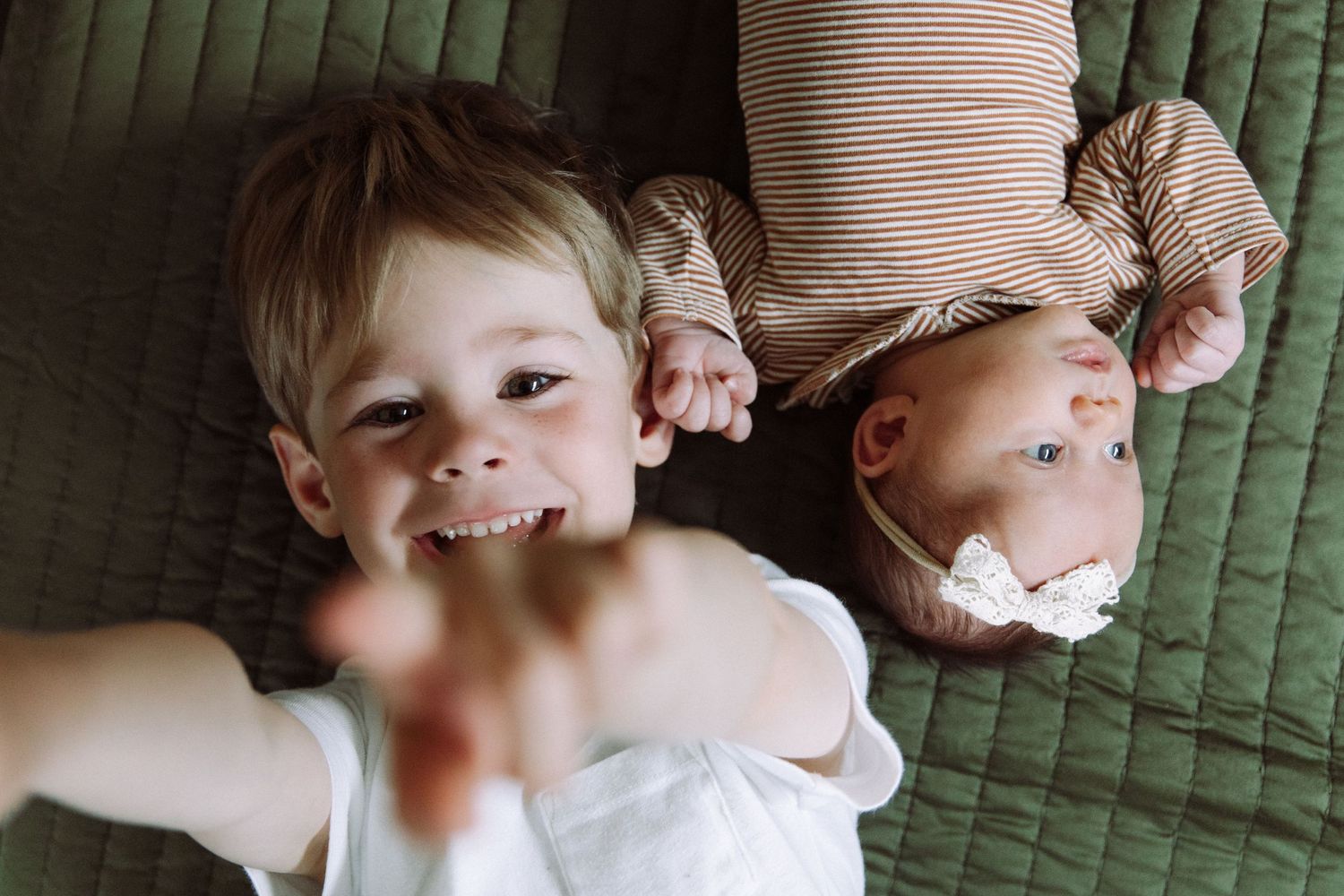 Playful overhead shot of children lying on green textured fabric.