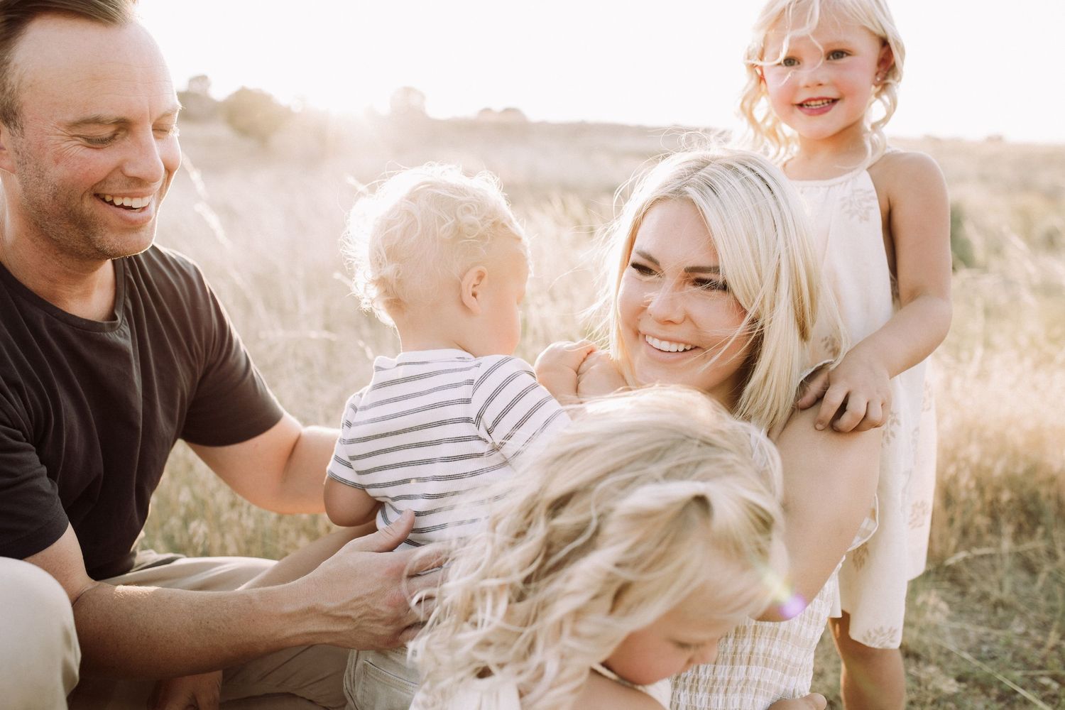 Family photoshoot in a sunlit field with warm golden hour lighting and natural poses.