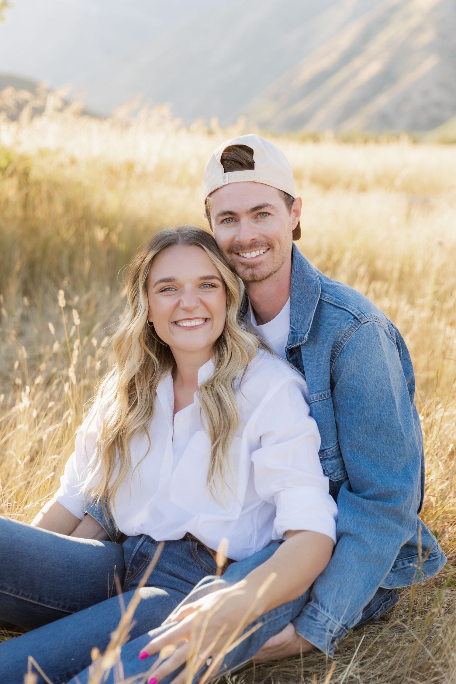 A couple relaxes in a sunny meadow with mountains visible in the distance during golden hour.