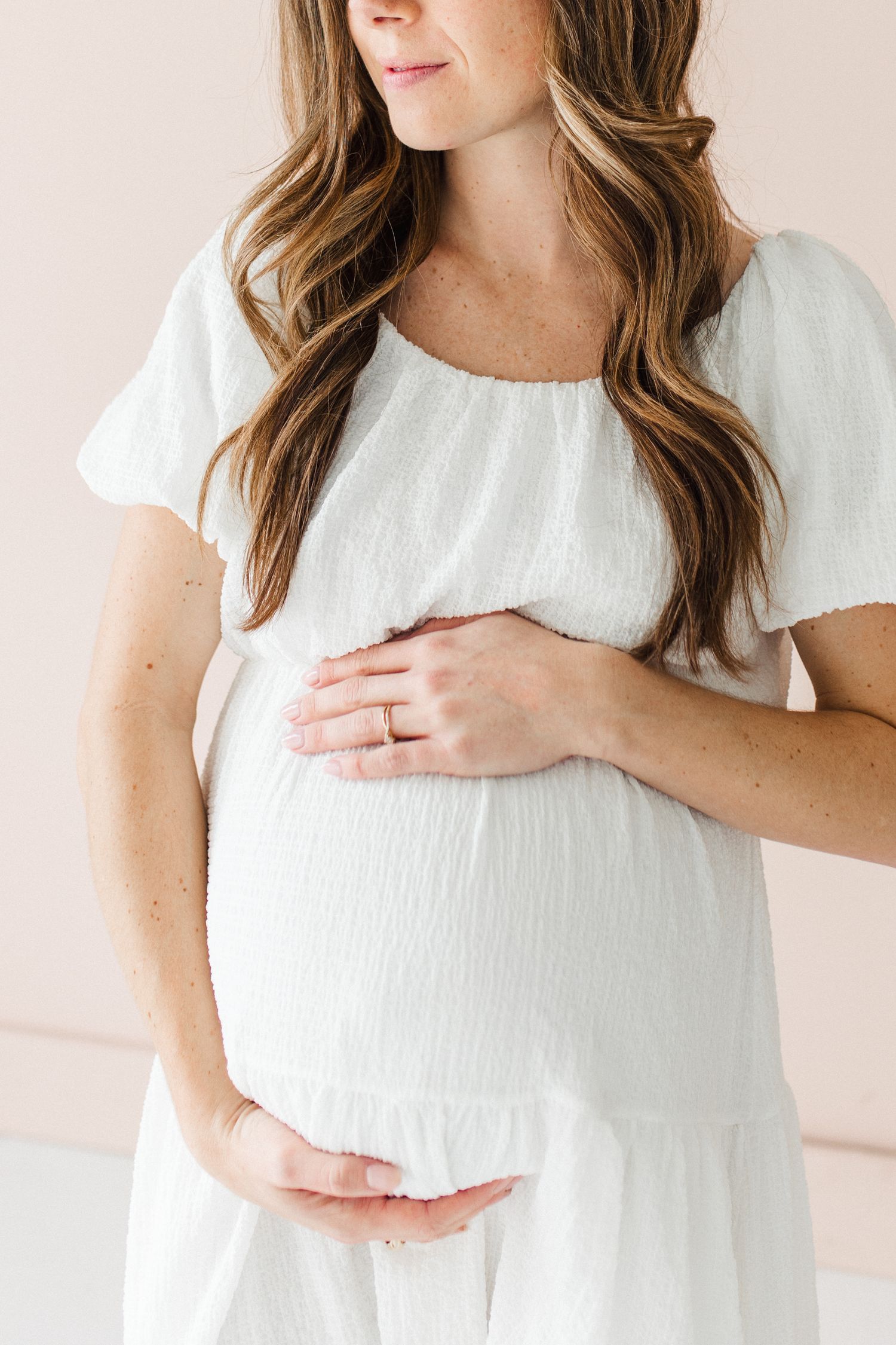 Close-up shots of expectant mother in white dress cradling baby bump with gentle hands.