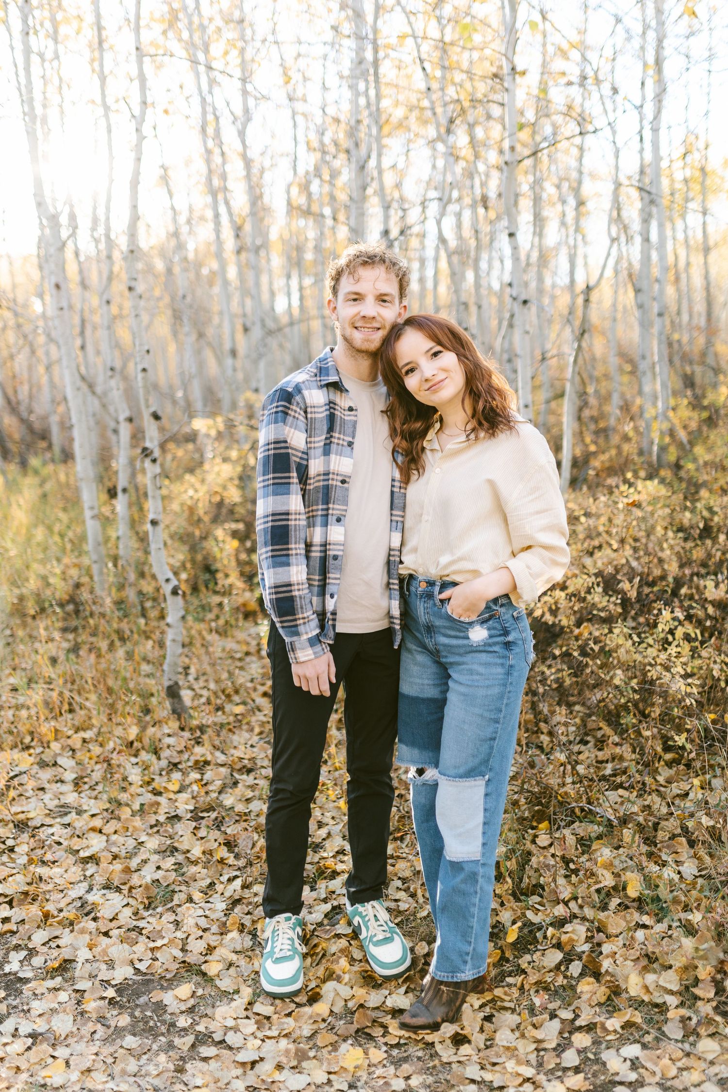 Couple poses playfully among golden aspen trees in autumn forest.