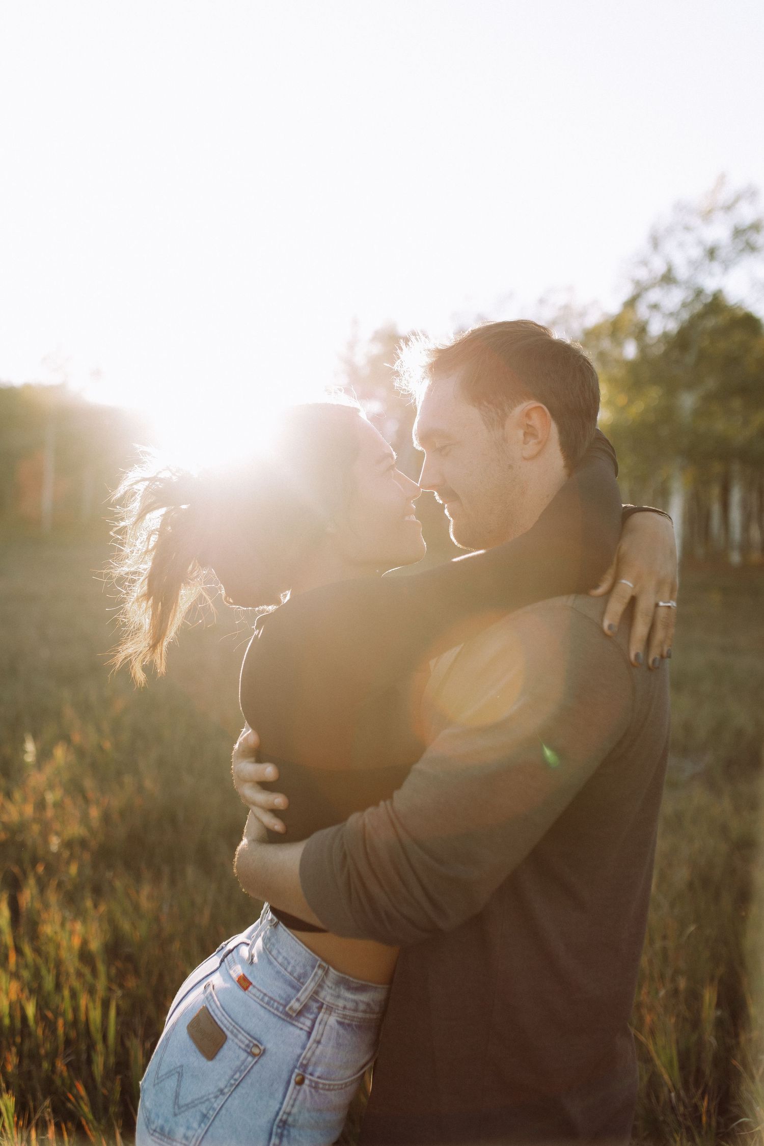 Intimate embrace captured in golden sunlight with romantic lens flare in an outdoor setting.