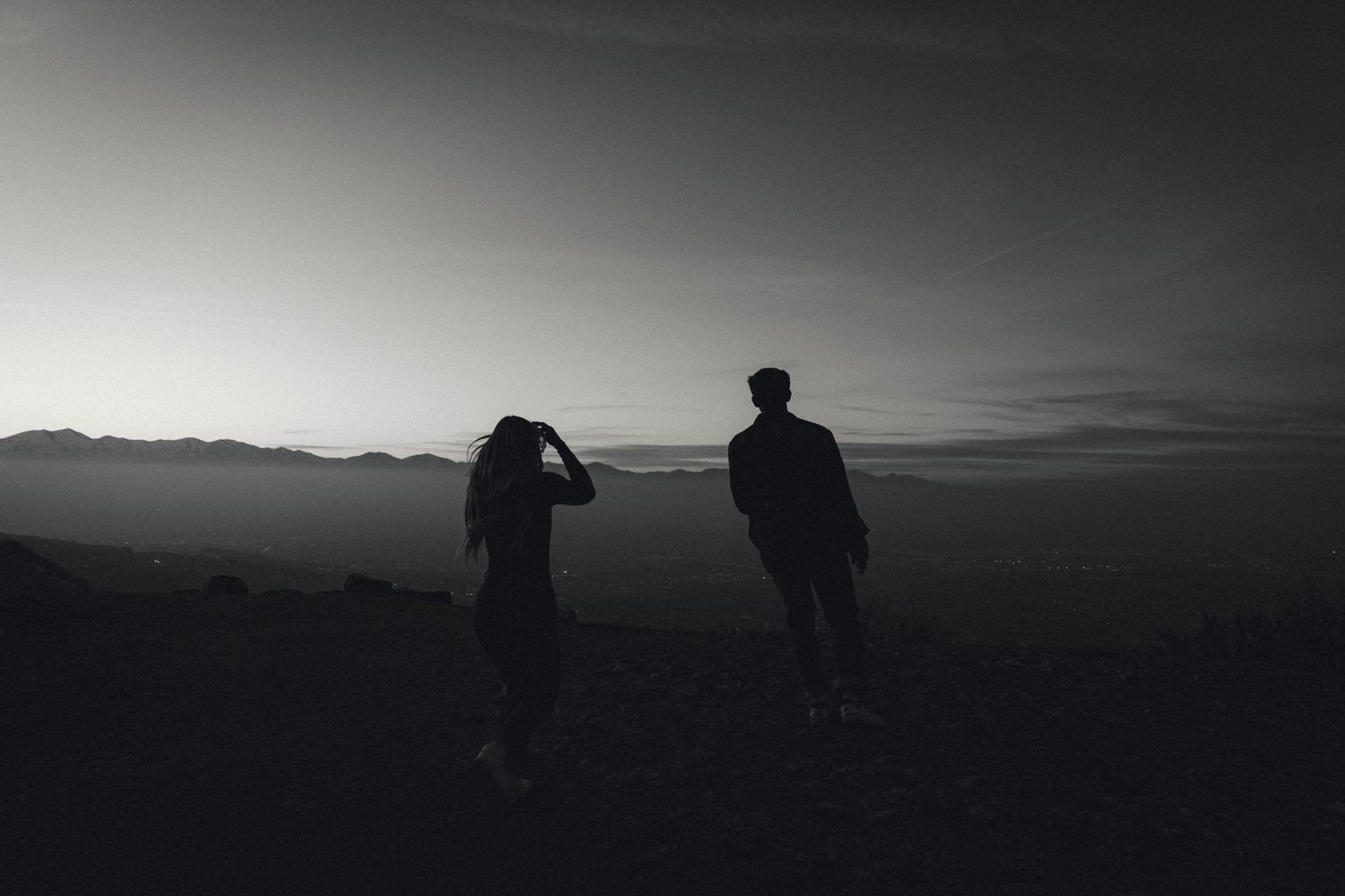 Silhouettes of two people standing on hilltop against dramatic mountain sunset.