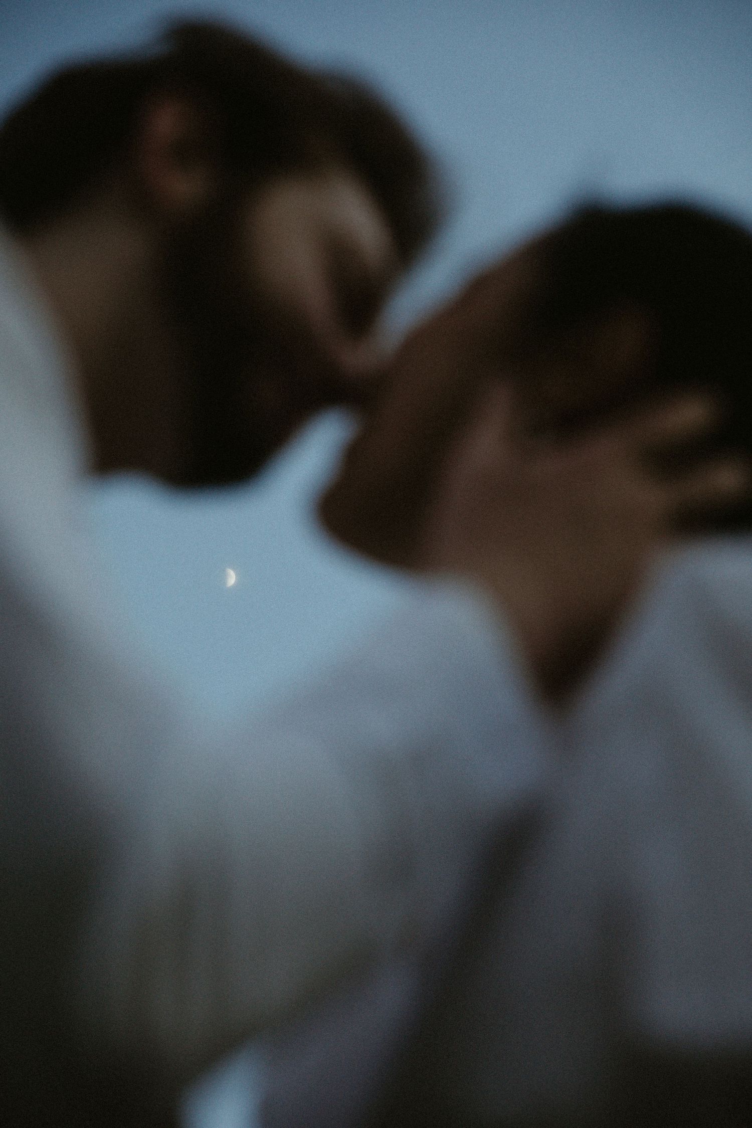 A silhouetted couple shares an intimate moment at dusk with a crescent moon visible.