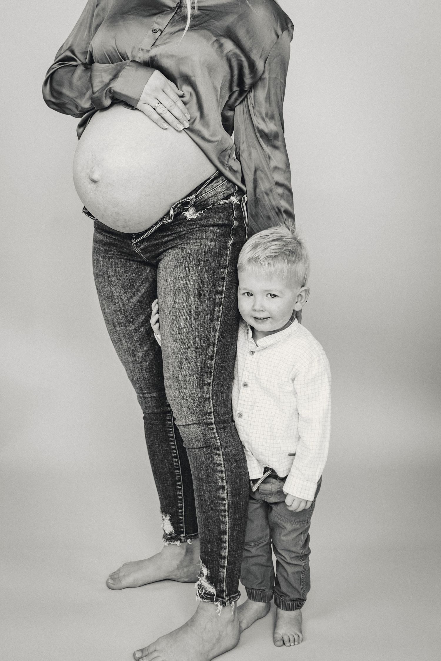 Black and white portrait of young child standing next to pregnant mother.