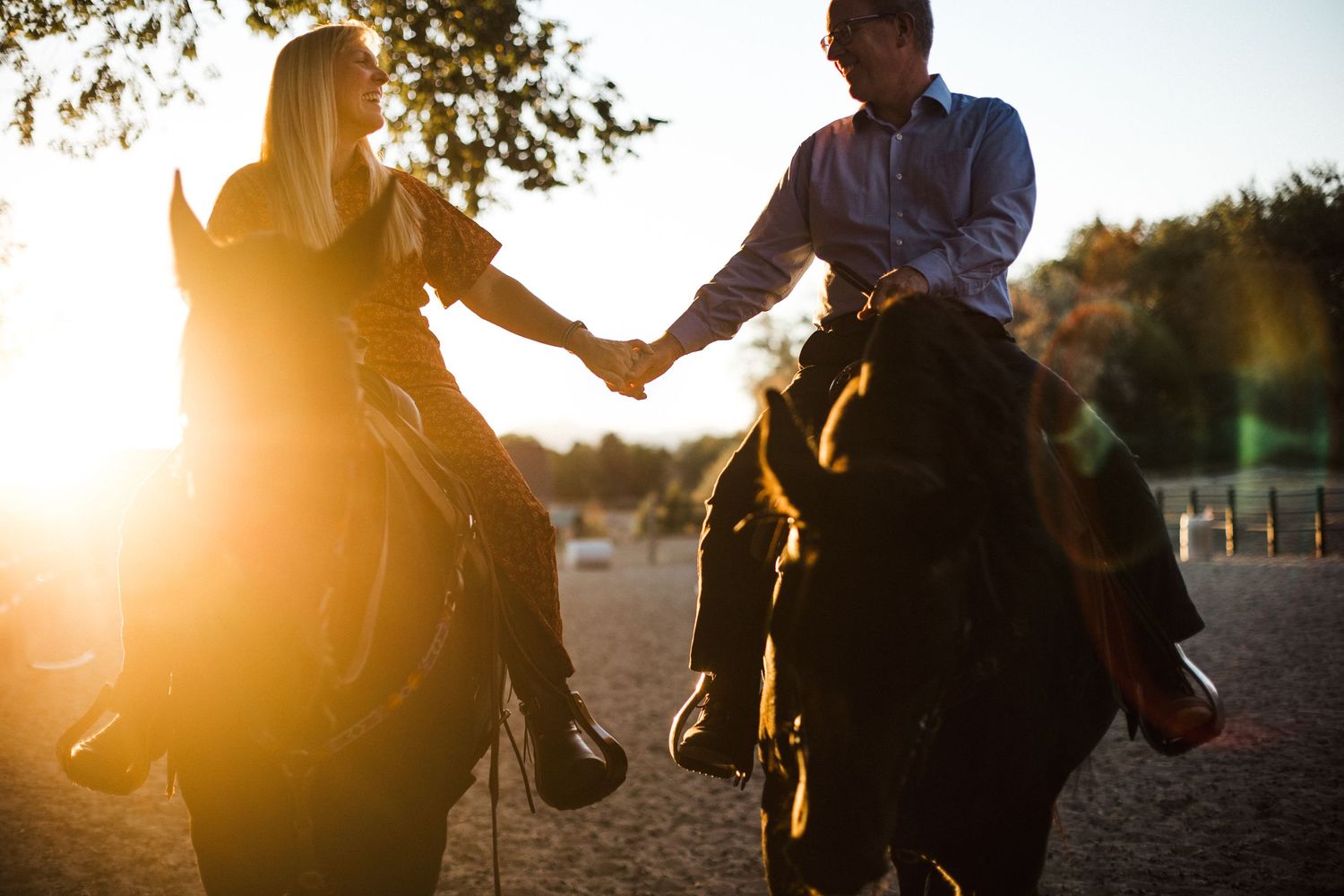 Couple holding hands while horseback riding together at sunset.