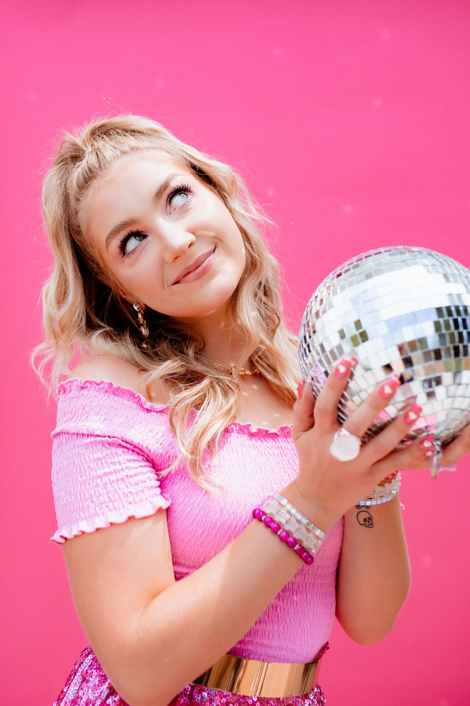 Playful pink studio shoot with silver disco ball and smocked crop top.
