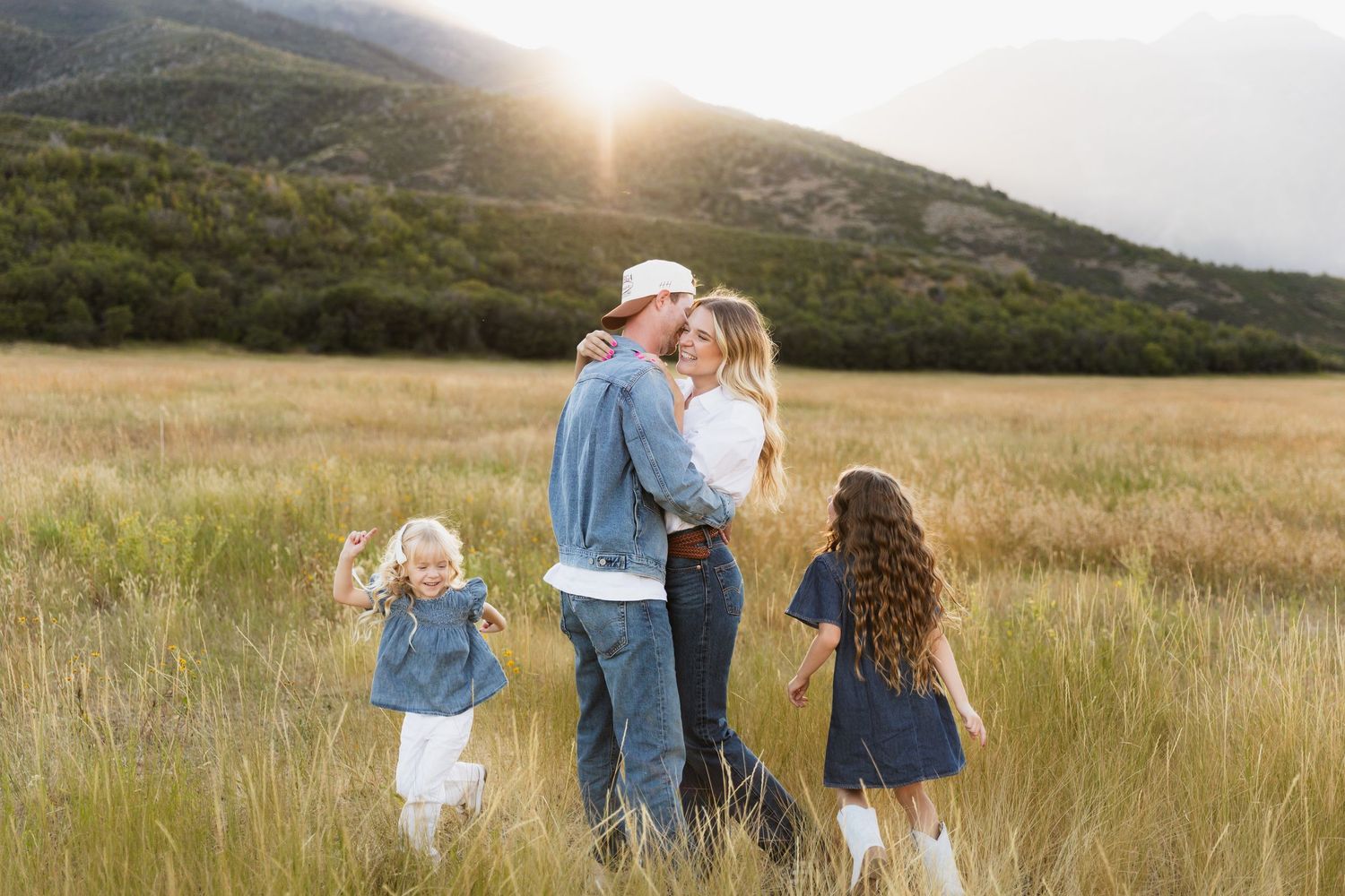 A group of people walk through a golden field at sunset with mountains in the background.