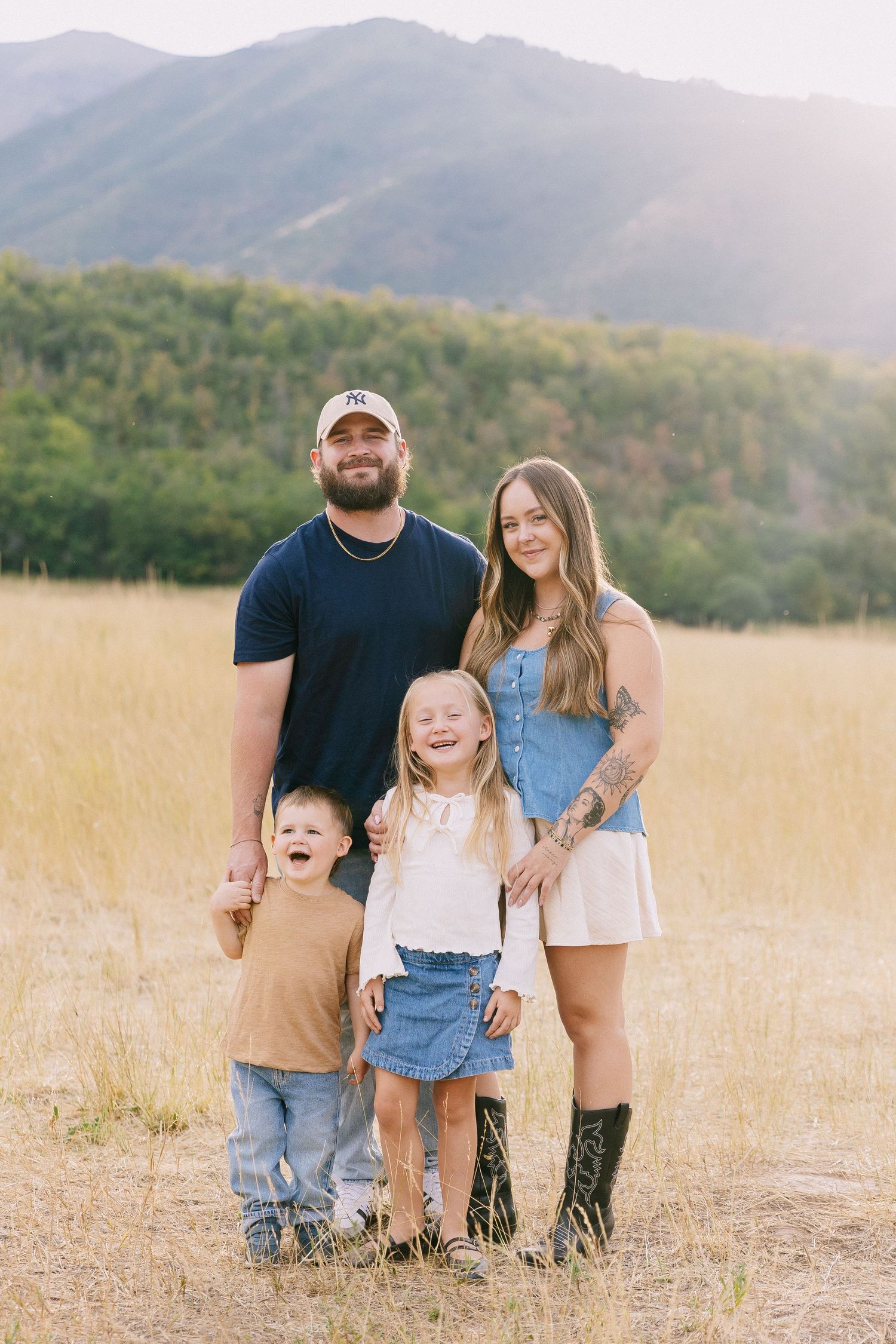 A family poses together in a golden field with mountains in the background on a sunny day.
