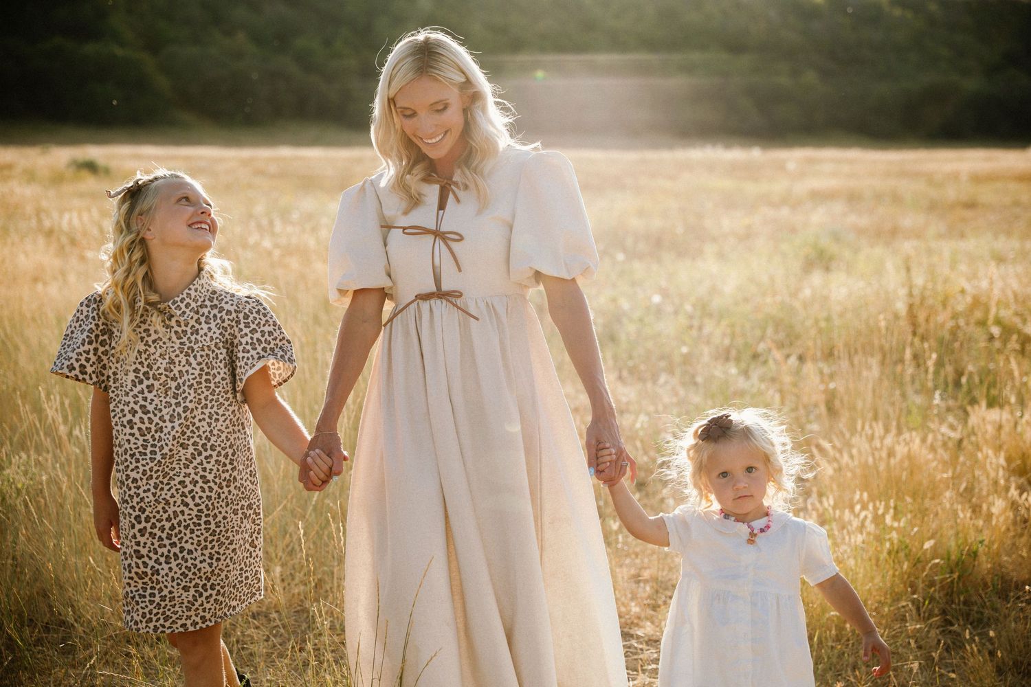 A group walks through a sunlit meadow at golden hour wearing white and floral dresses.