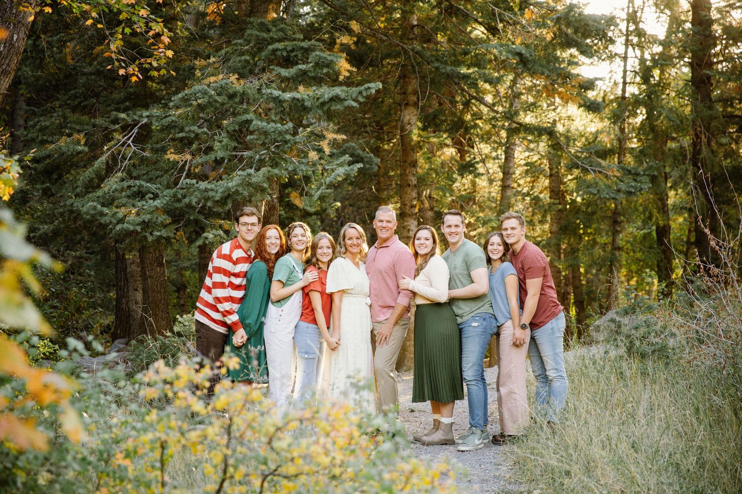 Group of people gathered on a forest trail during golden hour with sunlight filtering through trees.