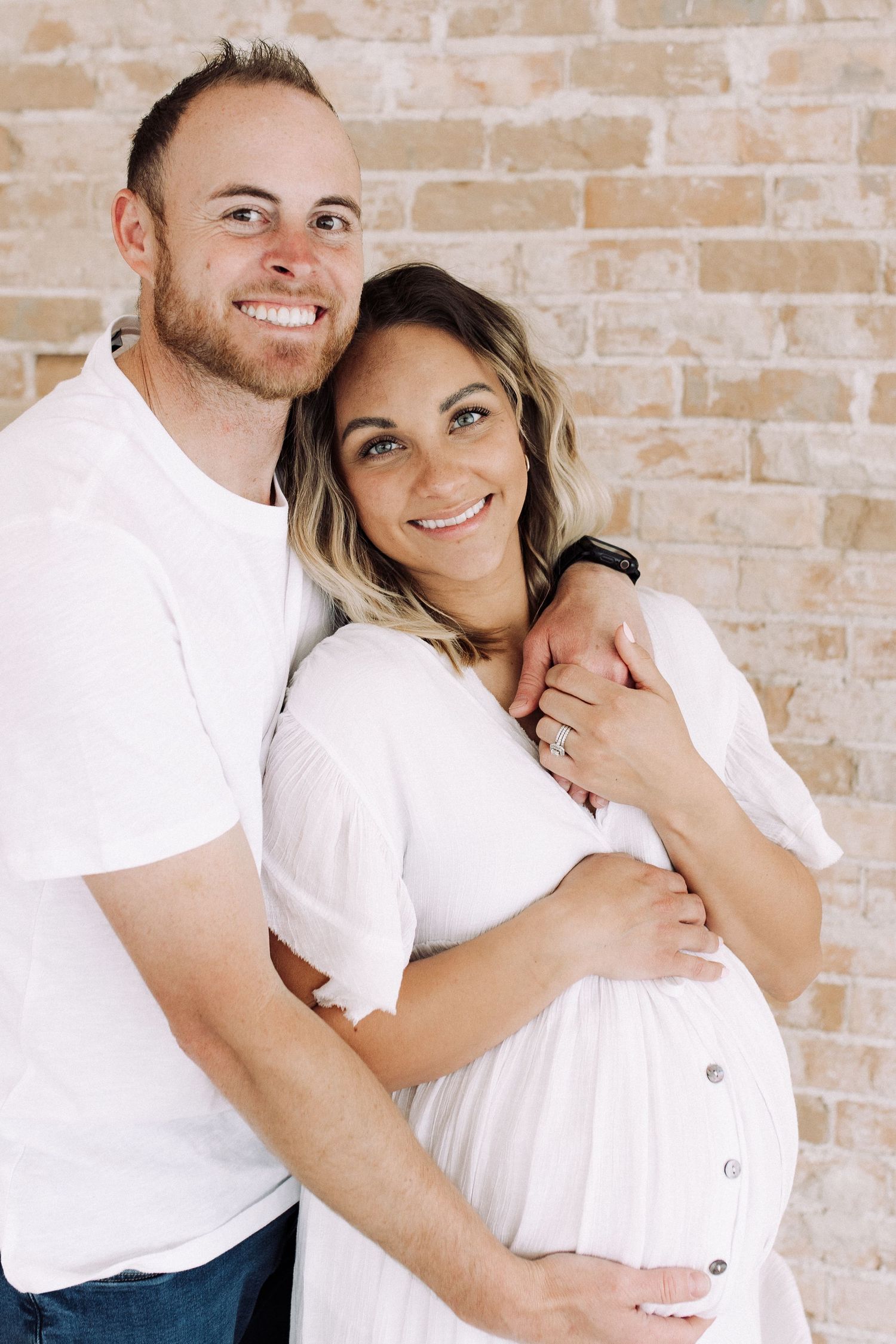 Couple poses against brick wall in matching white outfits for a photo series.