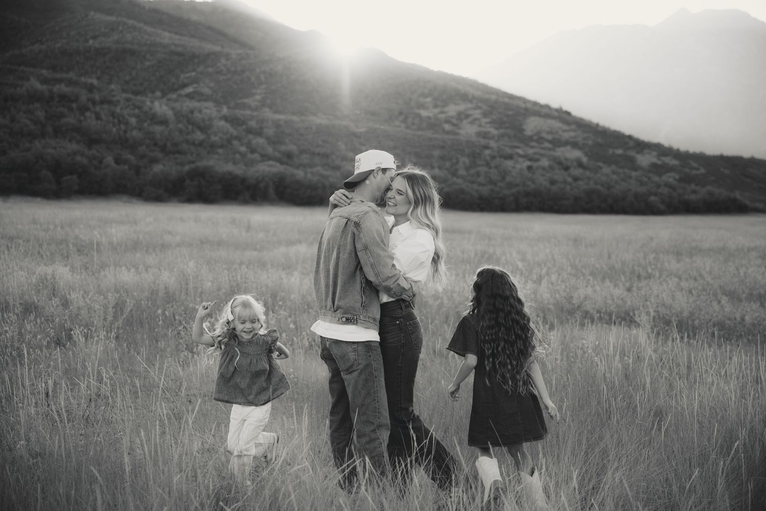 A black and white panoramic sequence of people walking through a grassy hillside field at sunset.