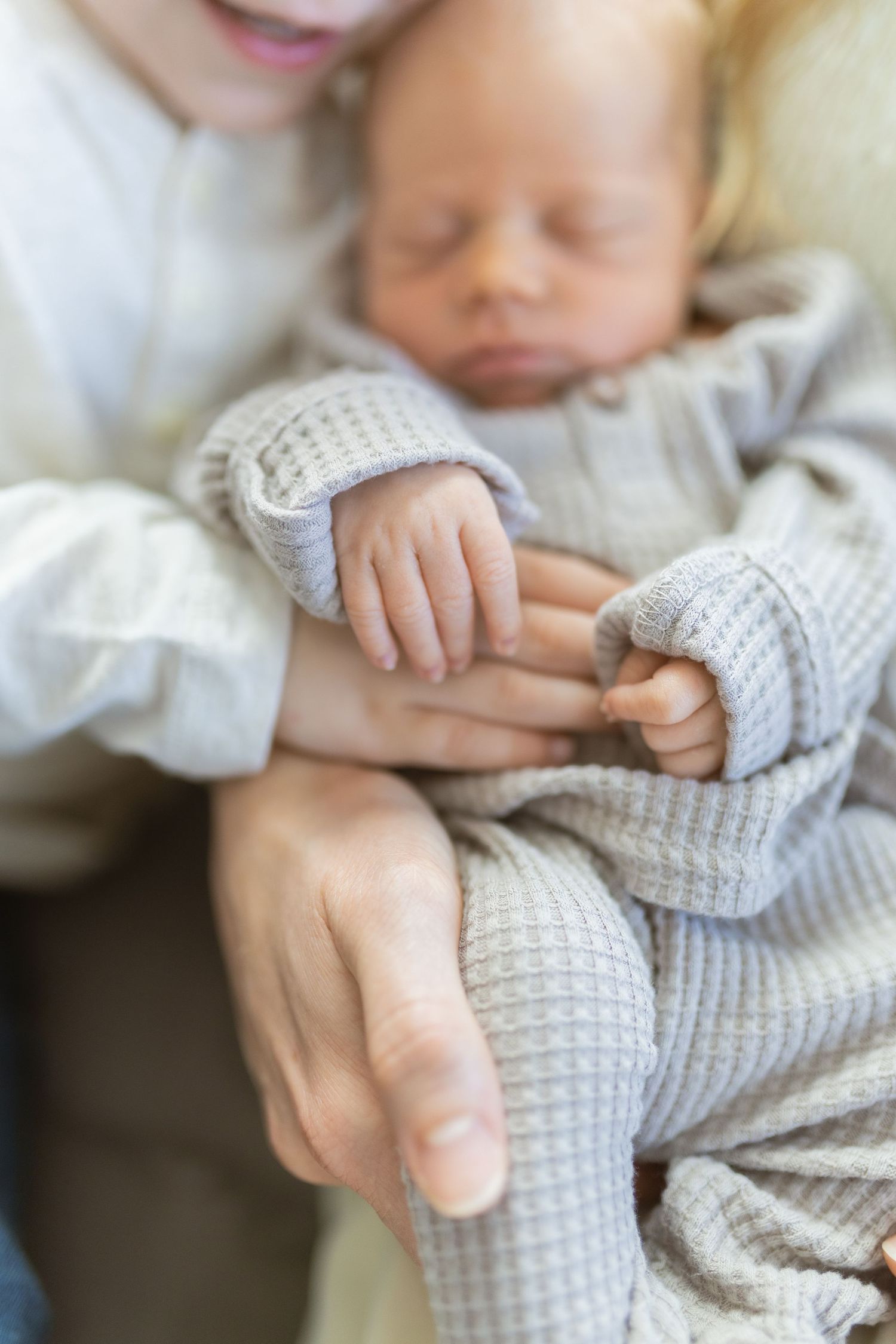 Newborn baby sleeping peacefully in a parent's arms, wearing a soft gray waffle-knit outfit.