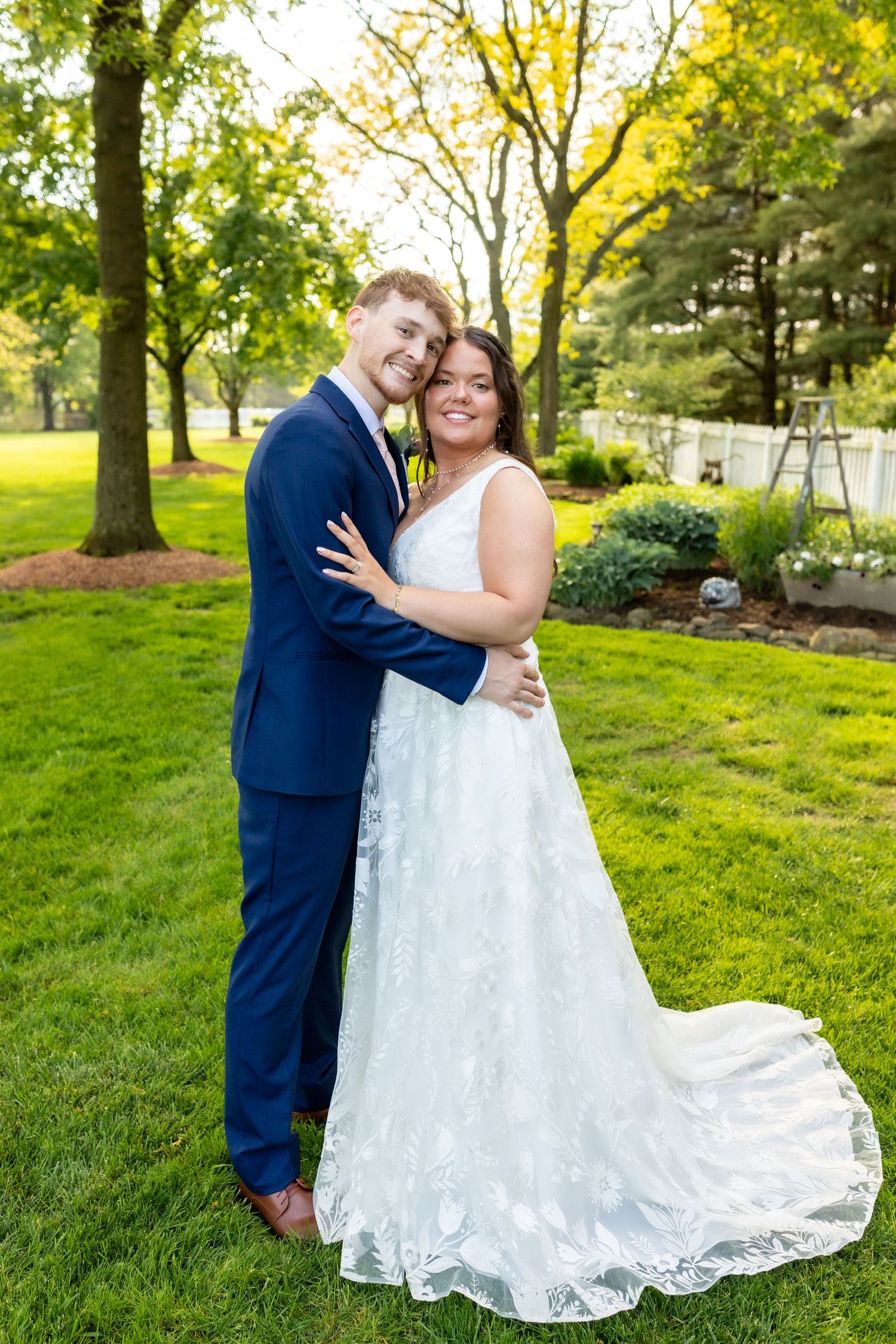 Happy bride and groom embracing in lush green garden on their wedding day.