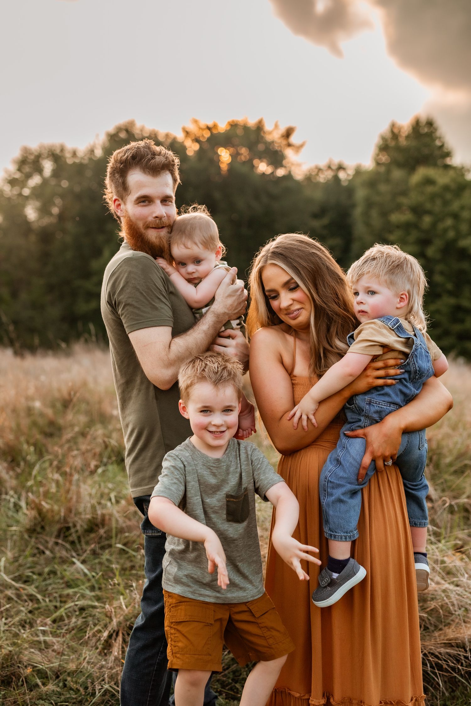 A candid family portrait at sunset in a field with parents and three young children.