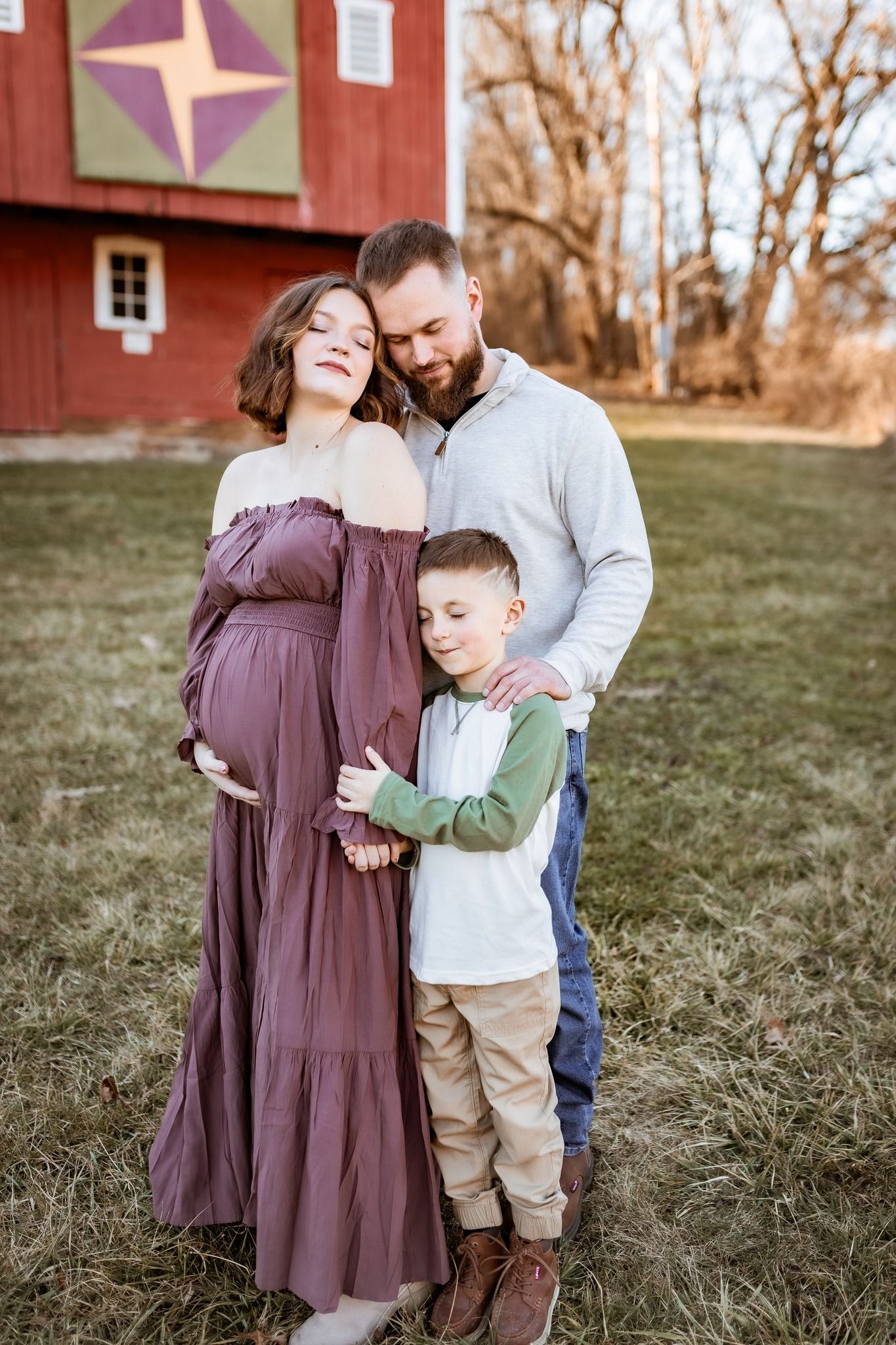 Family portrait in front of a red barn with a pregnant woman in purple dress.