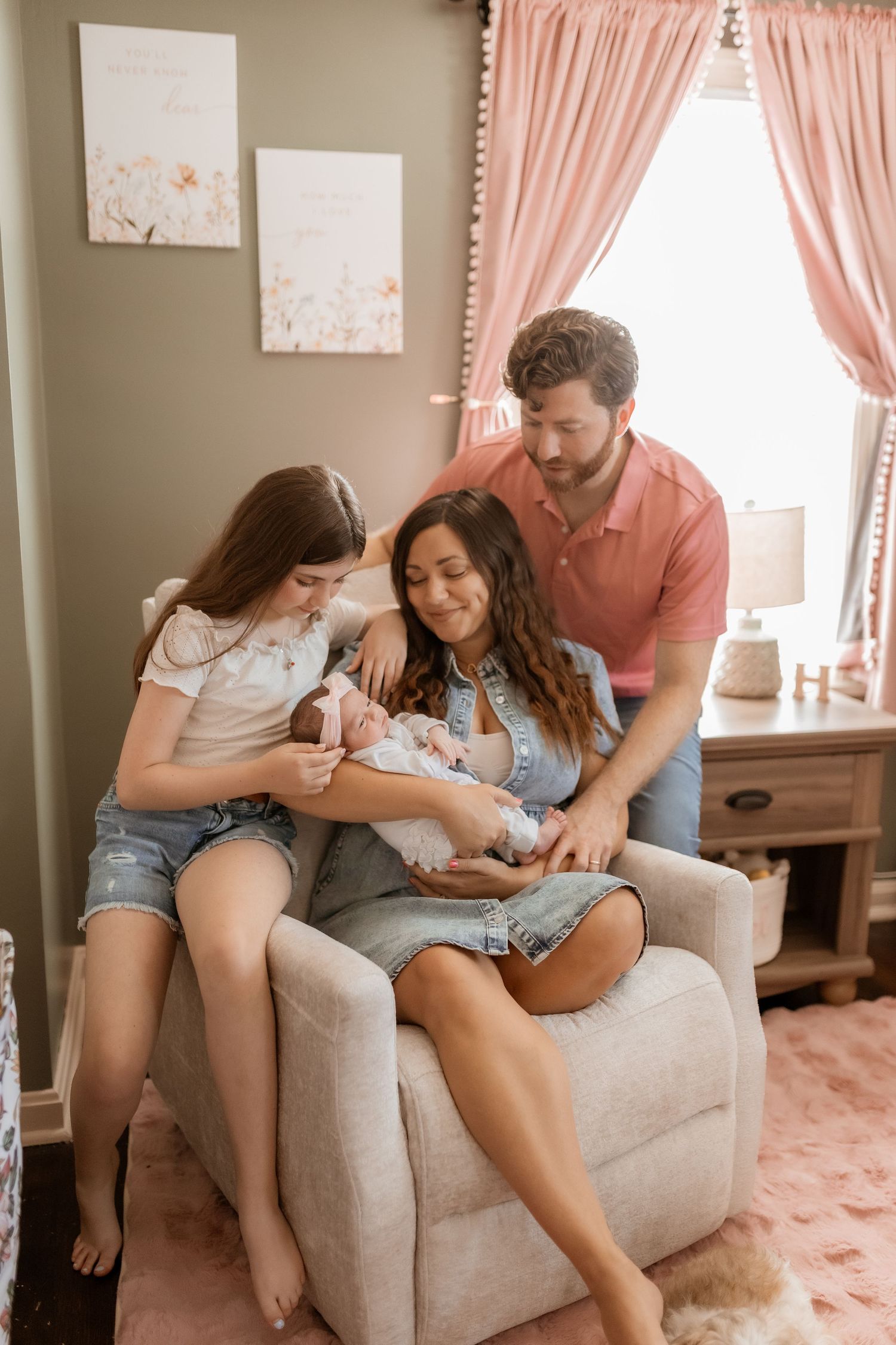 A family shares tender moments together on a cozy gray couch with pink curtains in the background.