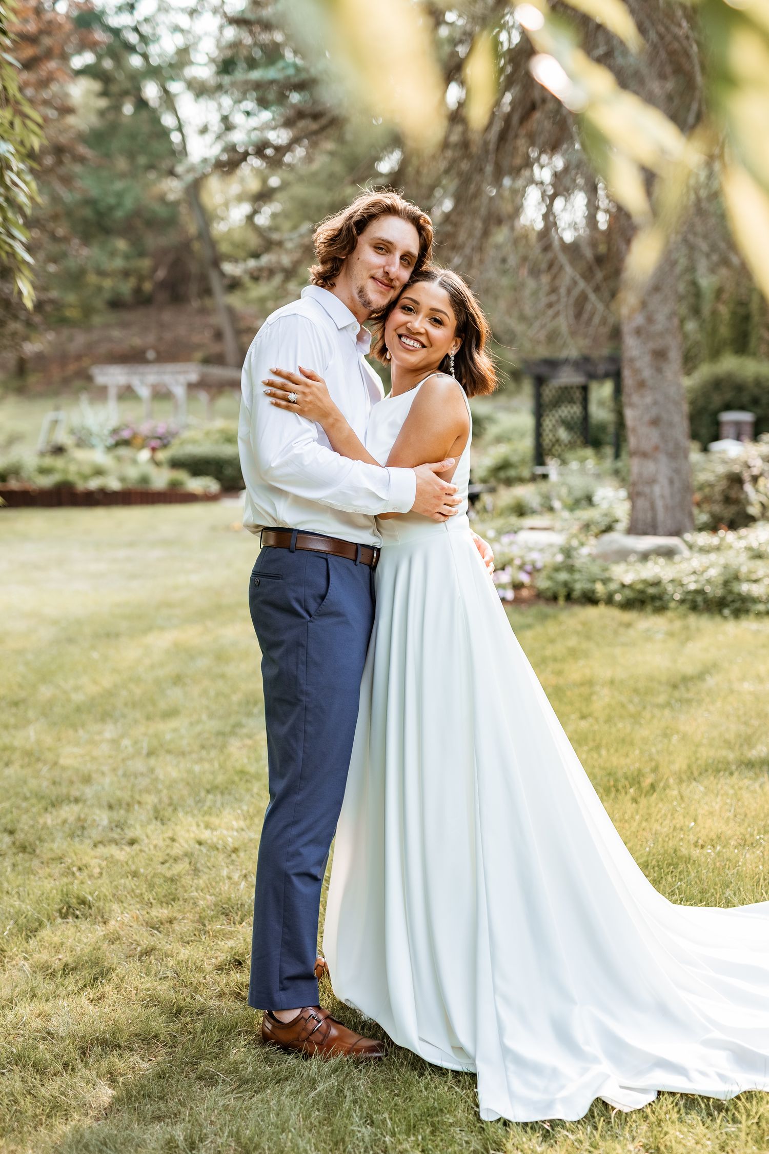 Elegant wedding couple embracing in a garden setting with a flowing white gown and classic attire.
