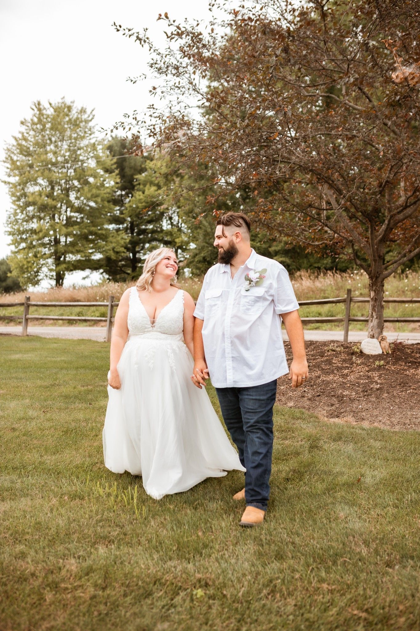 A couple walk hand in hand through a grass field on their rustic outdoor wedding day.