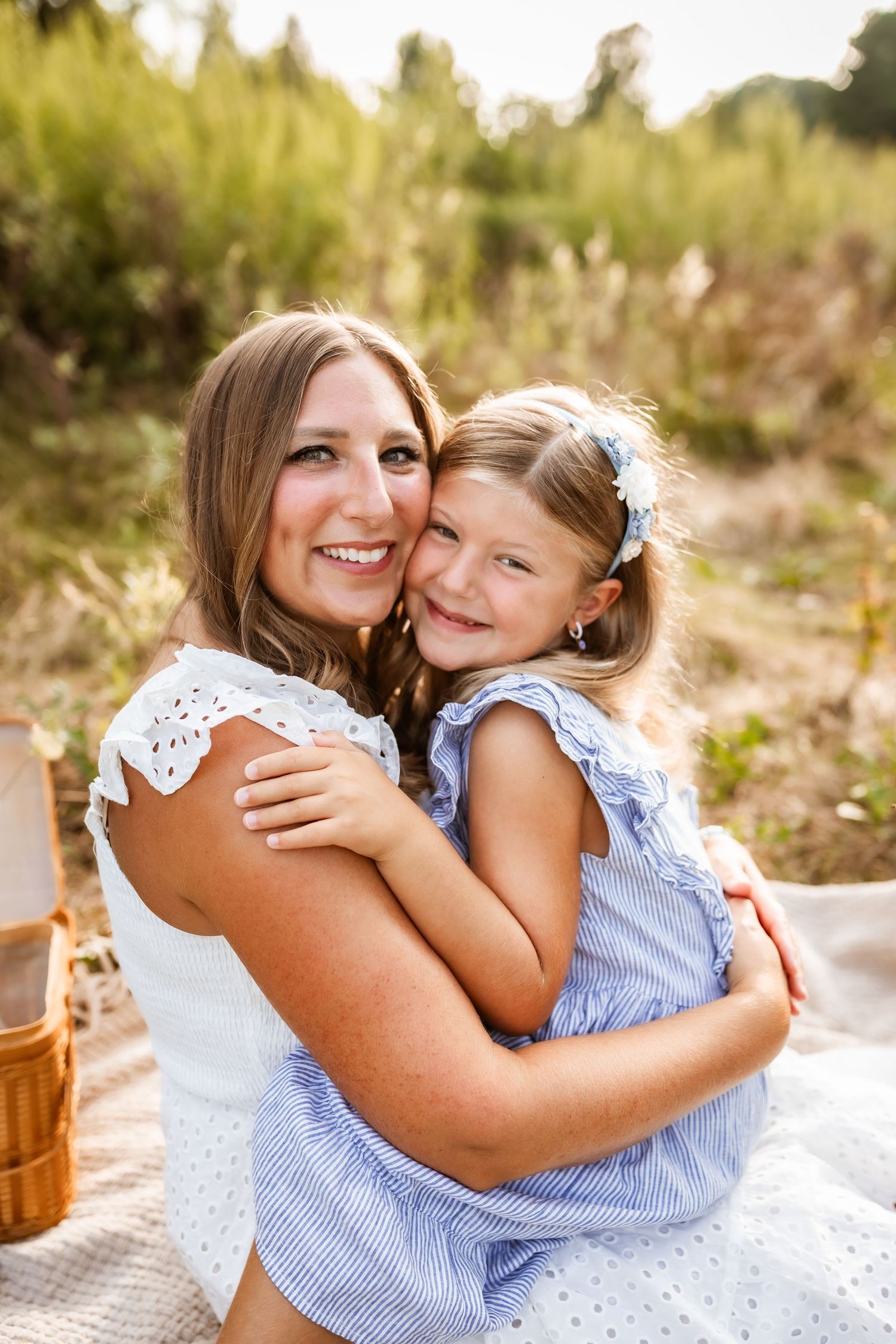 Two people share a warm embrace while sitting on a picnic blanket outdoors in golden sunlight.