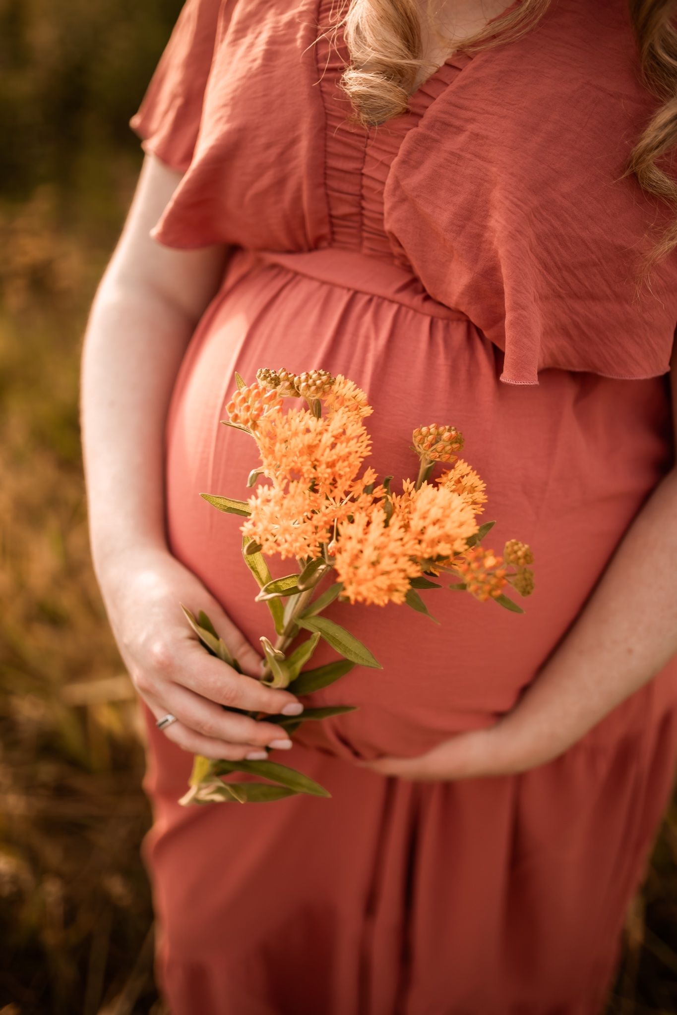 A maternity photo featuring a coral dress and orange wildflowers against a sunset backdrop.