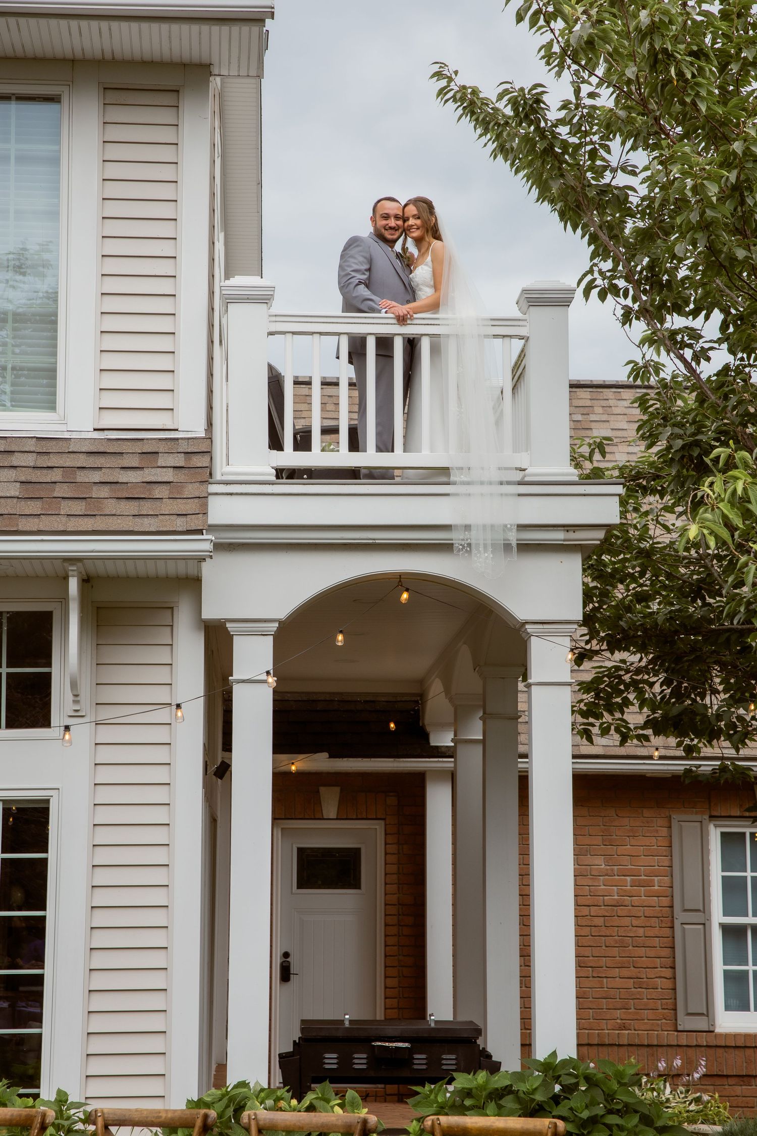 Bride and groom smiling together on a white balcony of an elegant colonial-style venue on their wedding day.