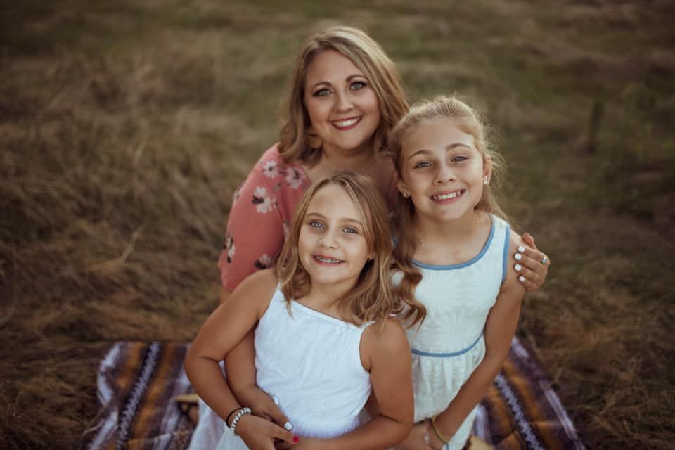 A family sits together on a blanket outdoors during a warm sunset portrait session in a rustic field.